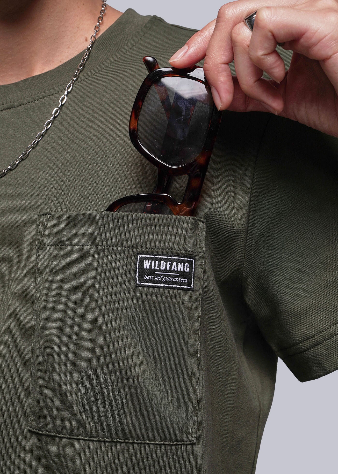 S=Person wearing a green t-shirt with a Wildfang logo on pocket, holding sunglasses.