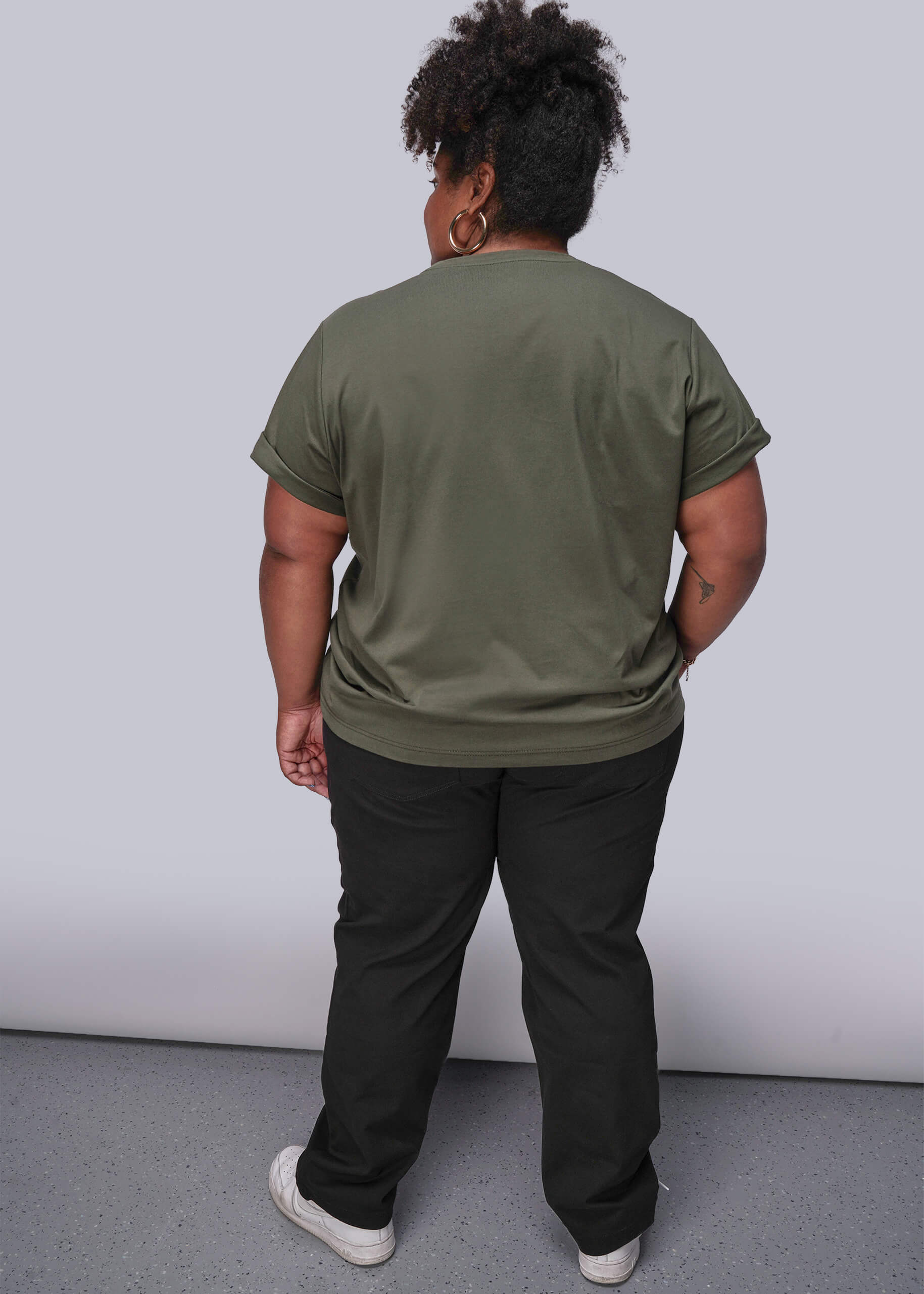 1X=Person wearing an olive green t-shirt and black pants against a white background
