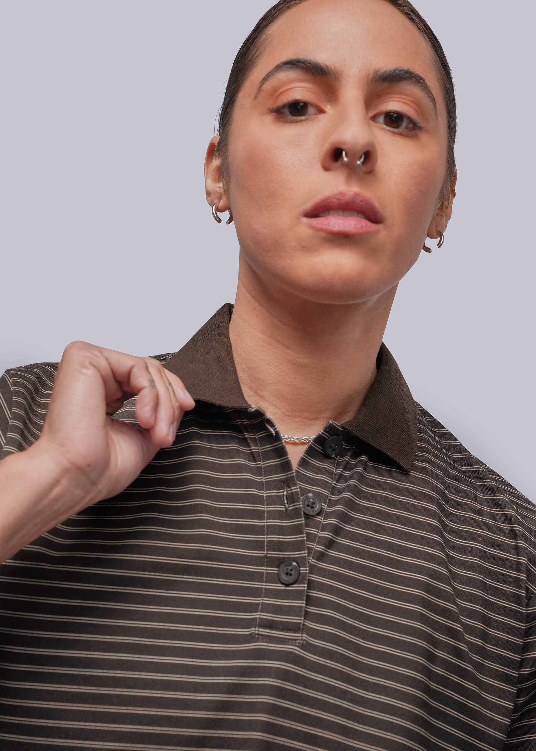 S=A close-up of a person wearing a brown and dark brown striped polo shirt against a light gray studio background.