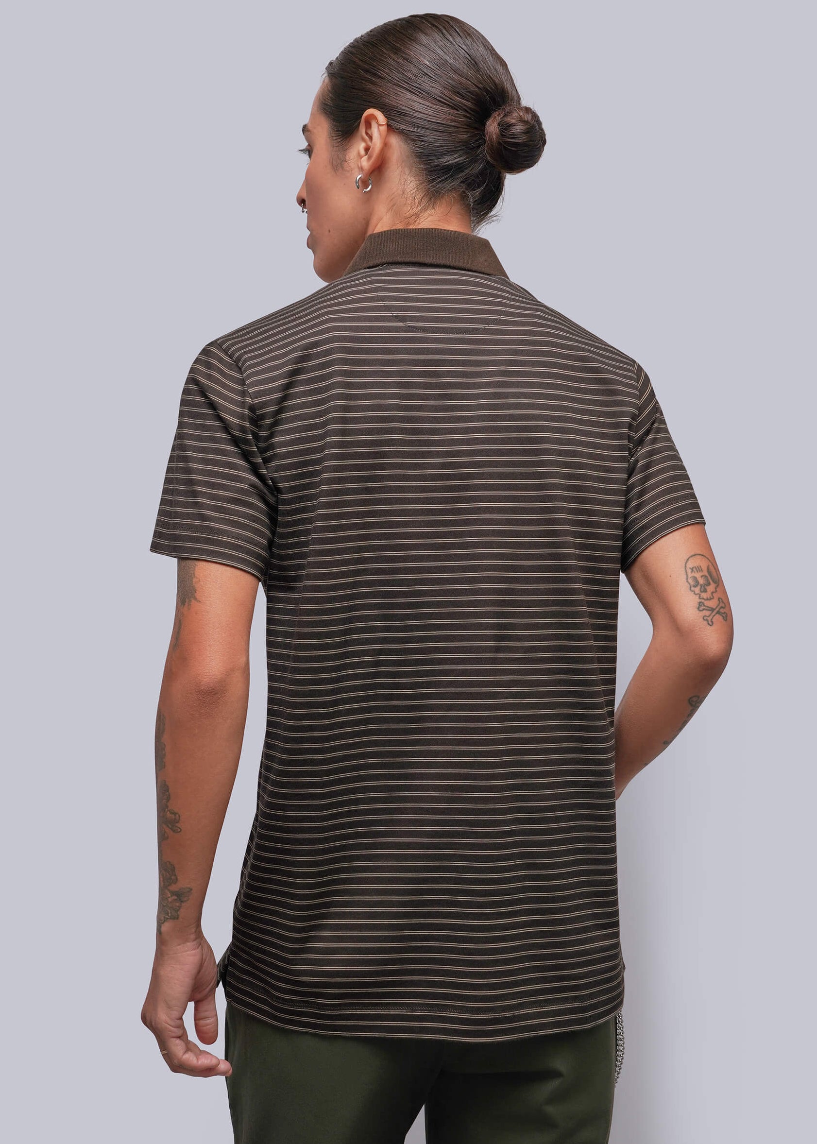 S=A person viewed from the back wearing a short-sleeve polo shirt with thin horizontal dark brown and black stripes, paired with dark olive pants, against a solid gray studio background.