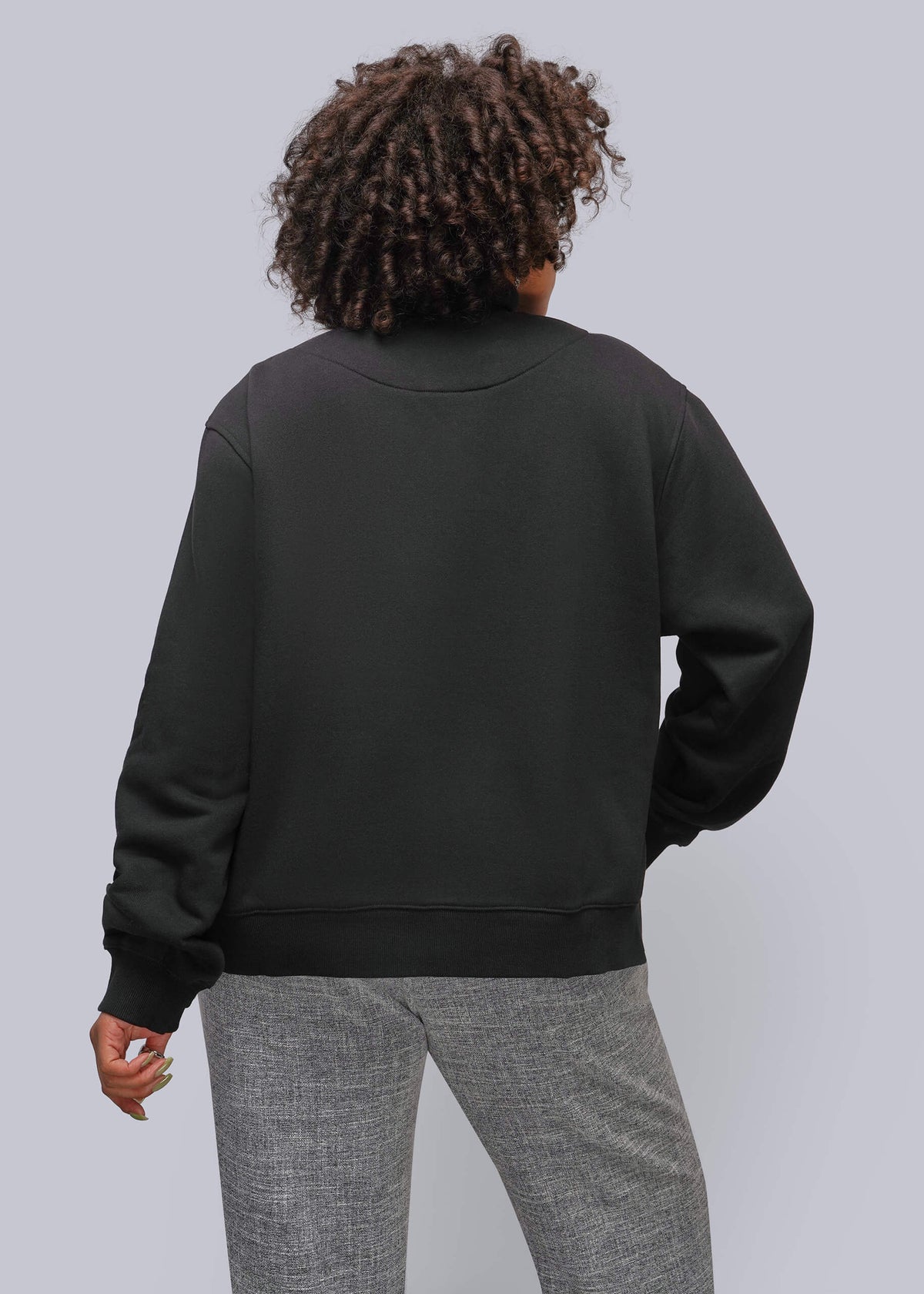 1X=A person shown from the back wearing a black crewneck sweatshirt and gray heather pants against a solid light gray studio background.
