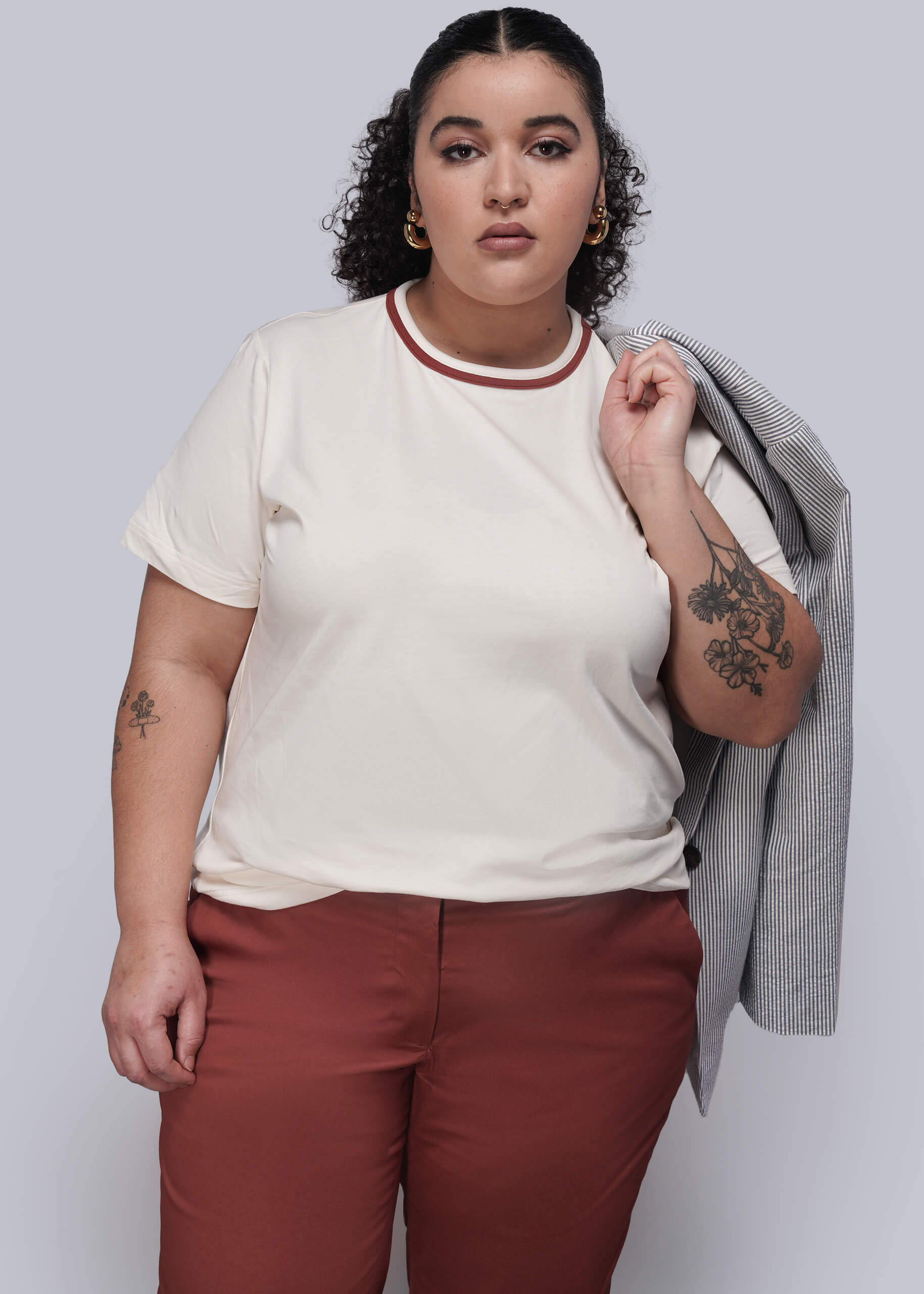 1X=Person wearing a white t-shirt with red trim and maroon pants, holding a gray jacket.