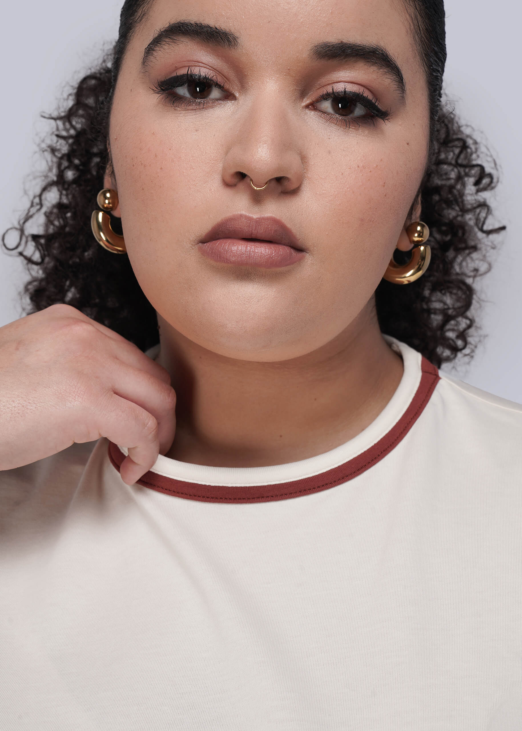 1X=Woman wearing gold hoop earrings and white shirt with red collar with a neutral background