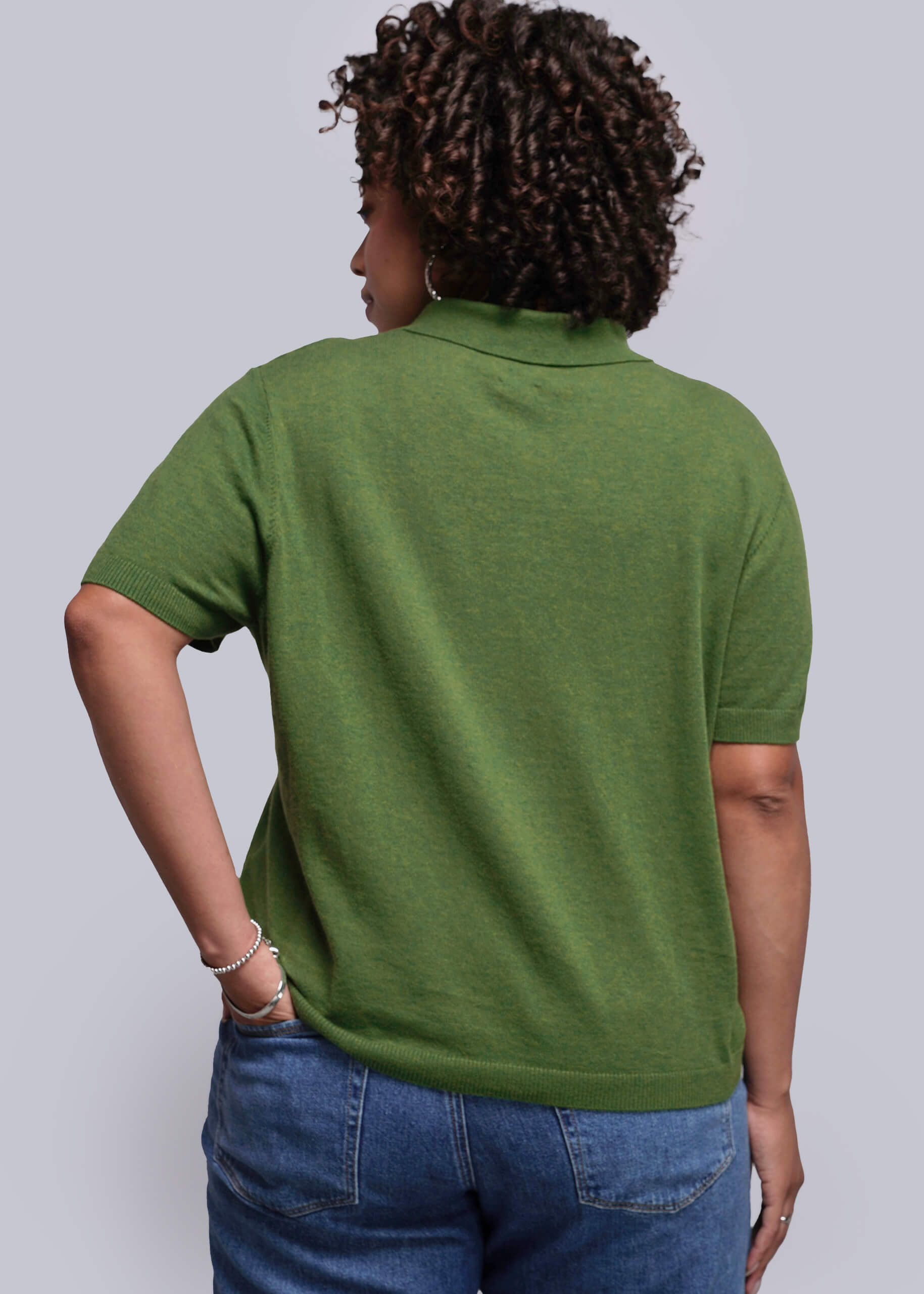 1X=Person wearing a green polo shirt and blue jeans against a plain background