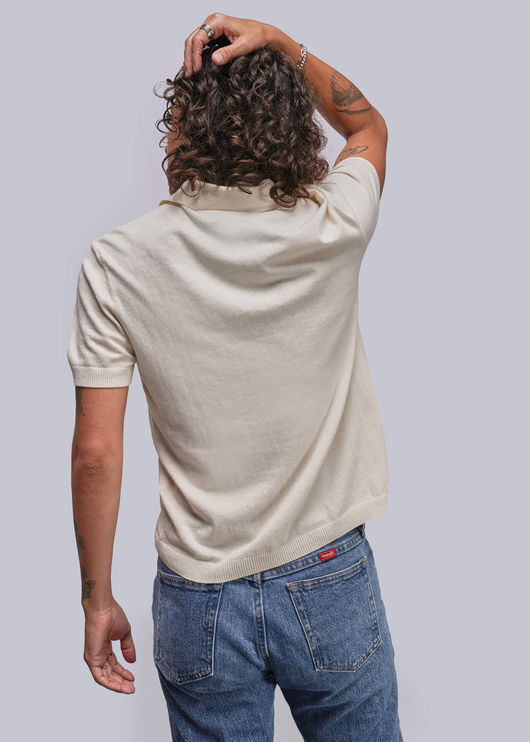 S=Person wearing a beige polo shirt and blue jeans against a plain background