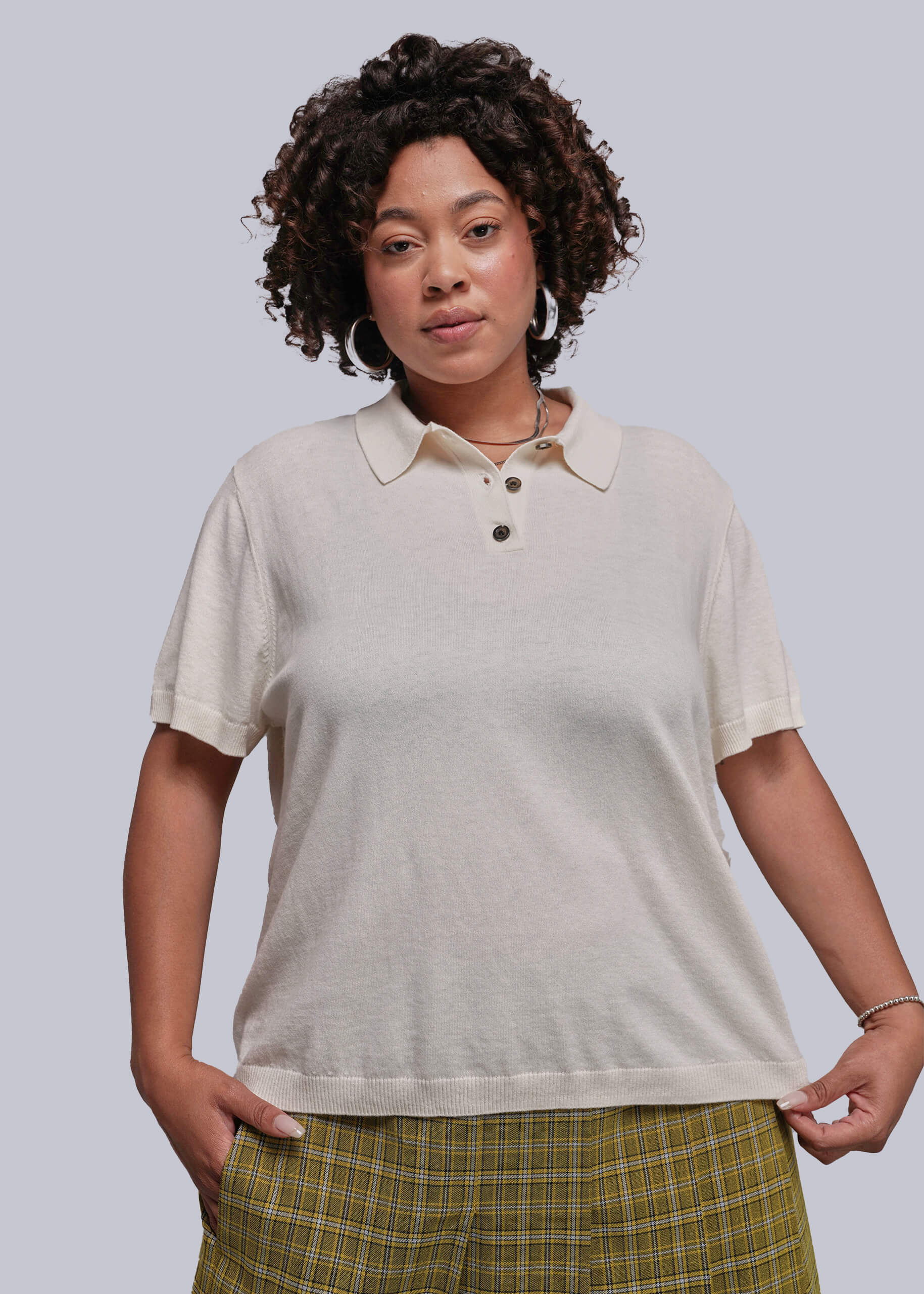 1X=Woman wearing a beige polo shirt and plaid pants against a plain background
