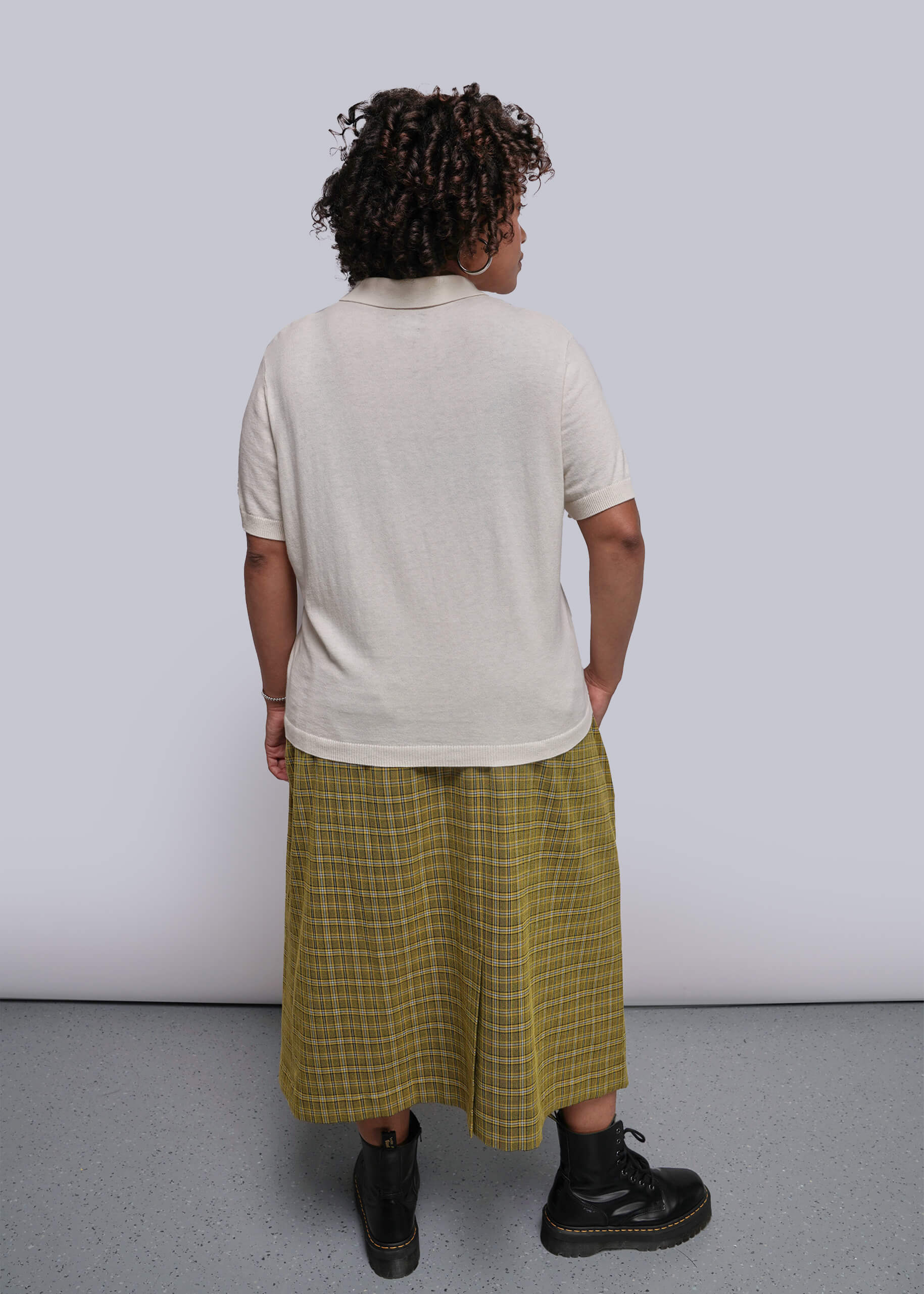 1X=Person wearing a white t-shirt and yellow plaid skirt against a plain background