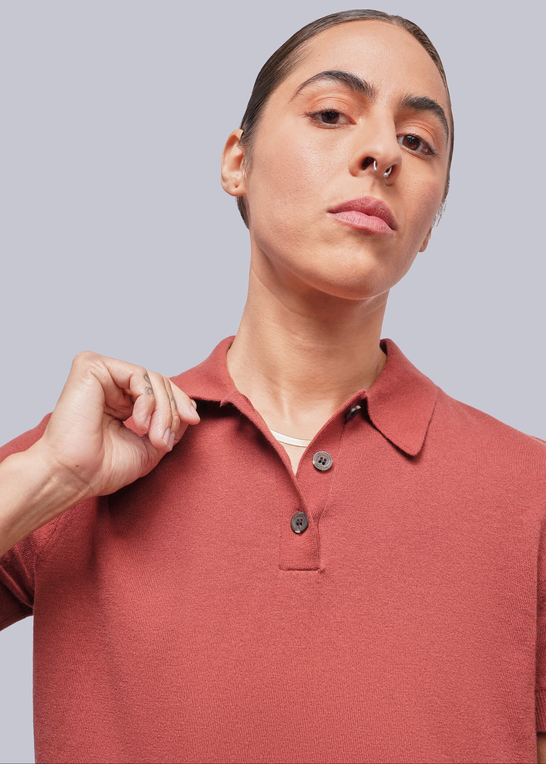S=A close-up of a model wearing a short-sleeve polo shirt in a muted terracotta color, set against a solid light gray background.