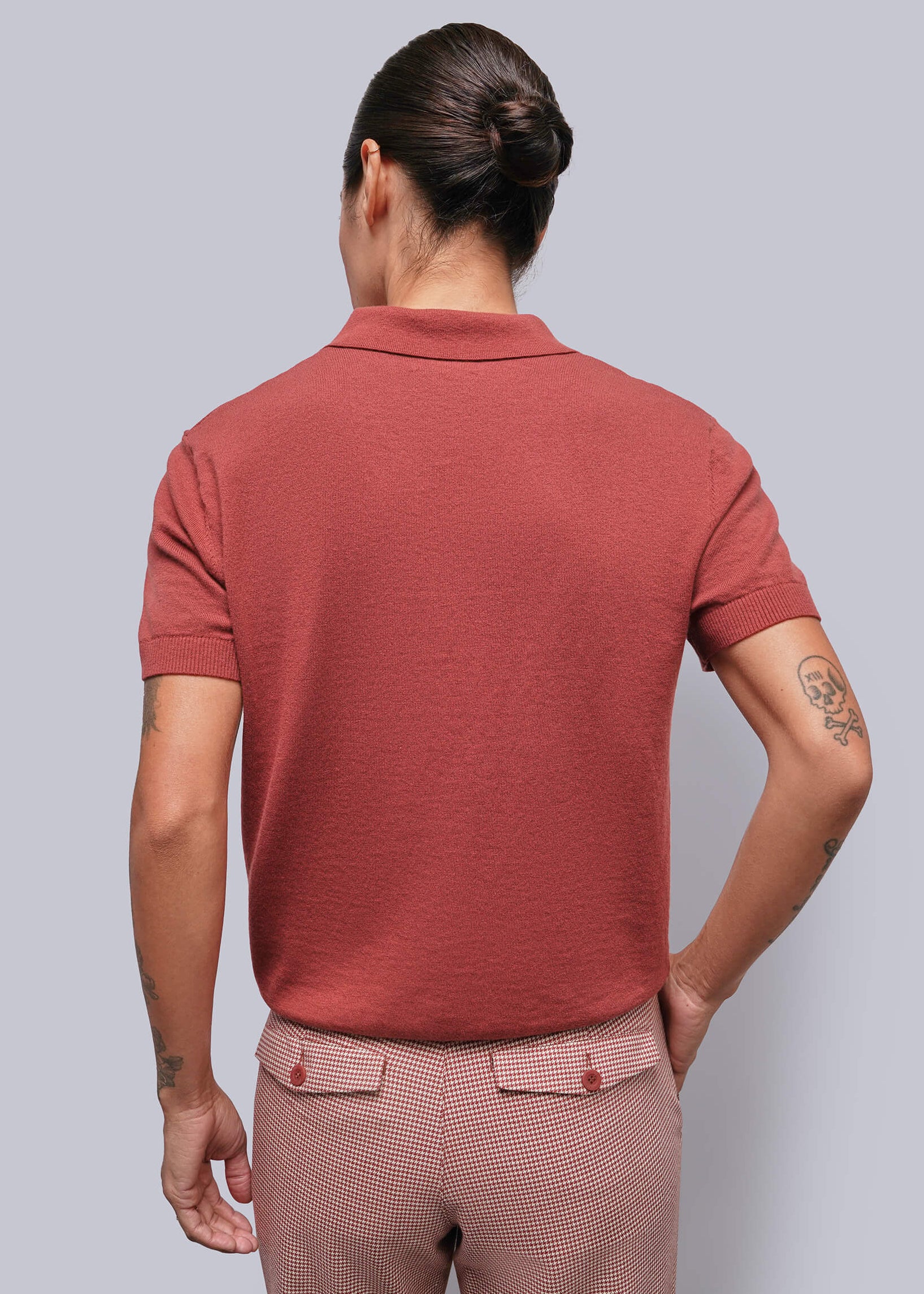 S=A person viewed from behind wearing a short-sleeve polo shirt in a muted terracotta red and matching patterned trousers, set against a solid light gray background.