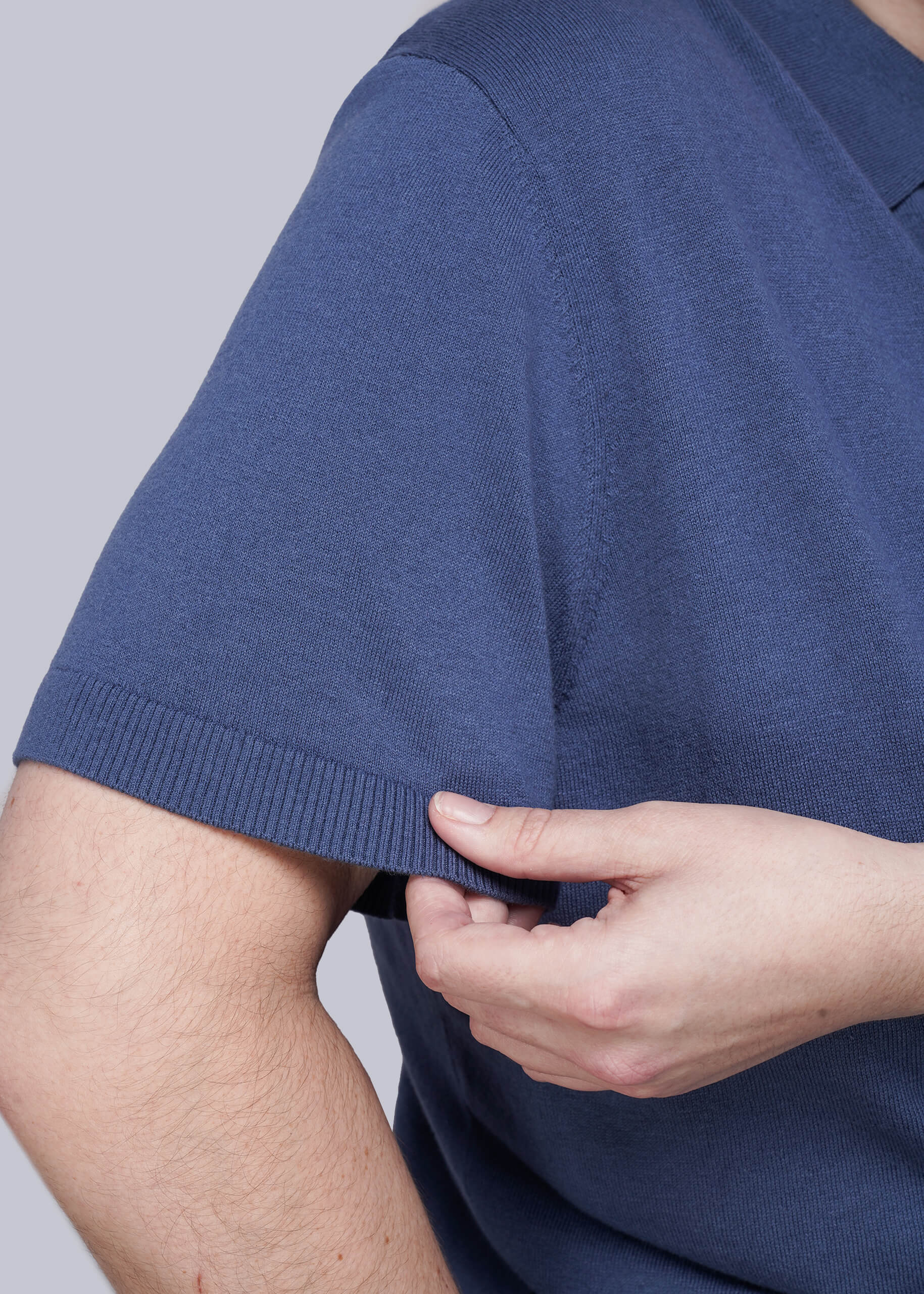 1X=Person wearing a blue shirt with a close-up of the sleeve and hand adjusting it against a gray background