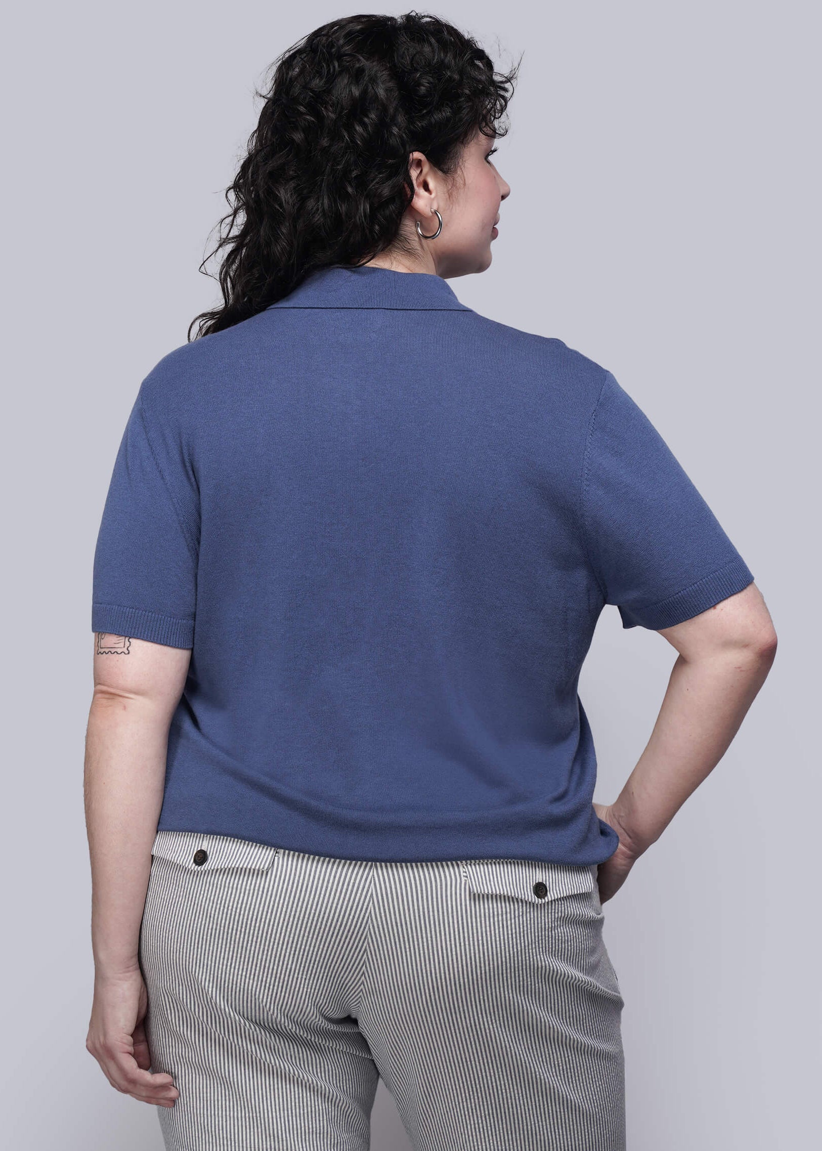 1X=Person wearing a blue polo shirt and striped pants against a plain background