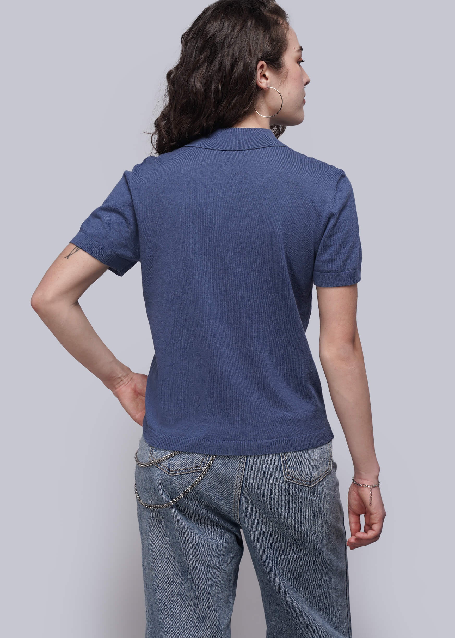 S=Person wearing a blue polo shirt and jeans against a plain background