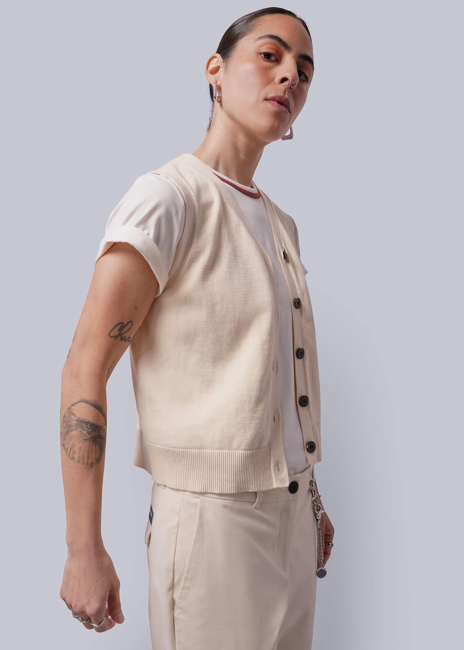 Person wearing a beige sweater vest over a white shirt, standing against a plain background.