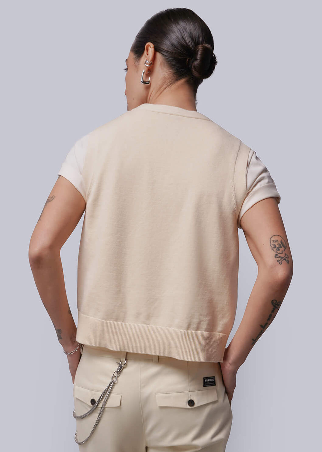 S=Person wearing a beige sweater vest with a plain background