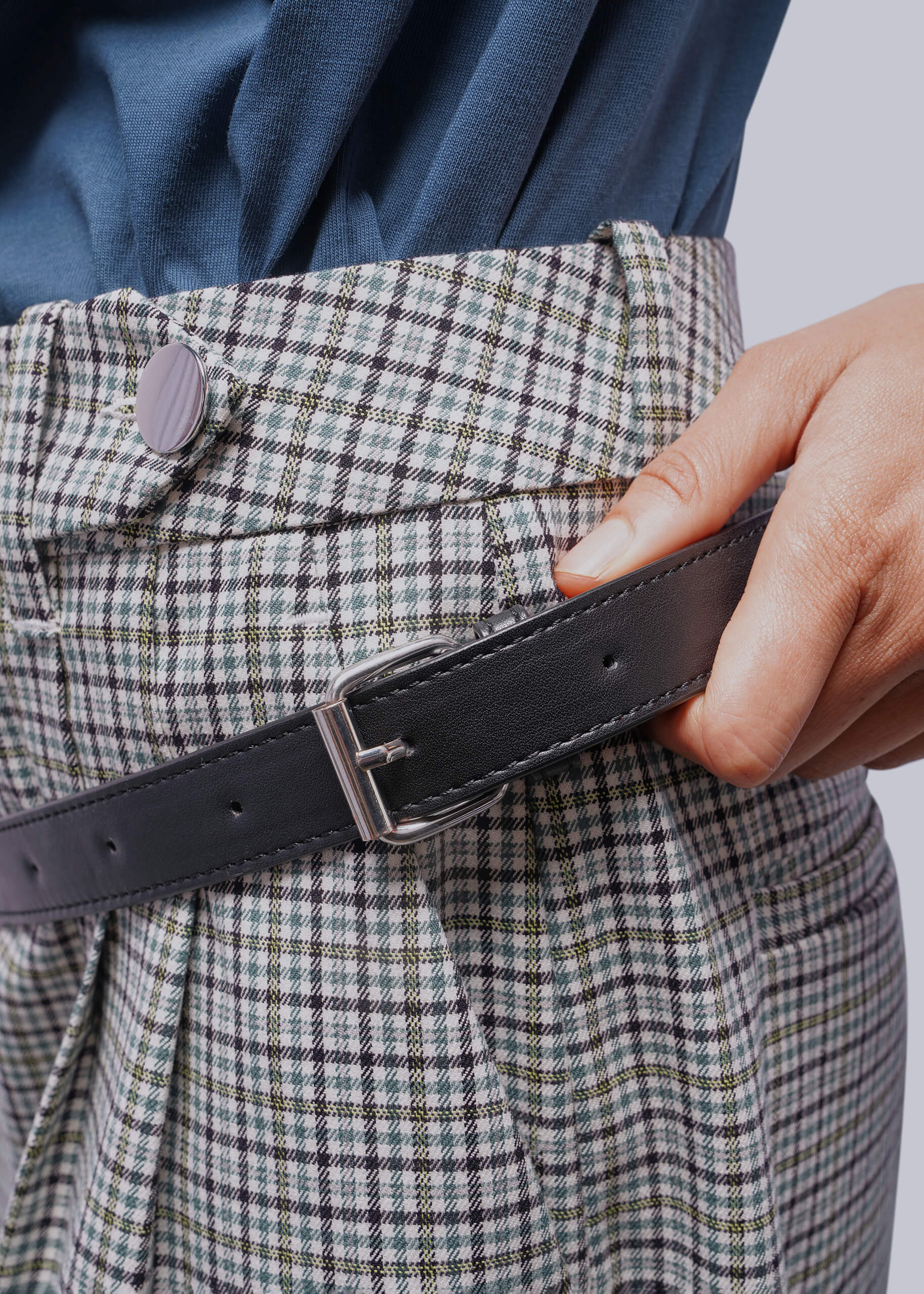 Person wearing a plaid jacket with a black belt and hand adjusting it.