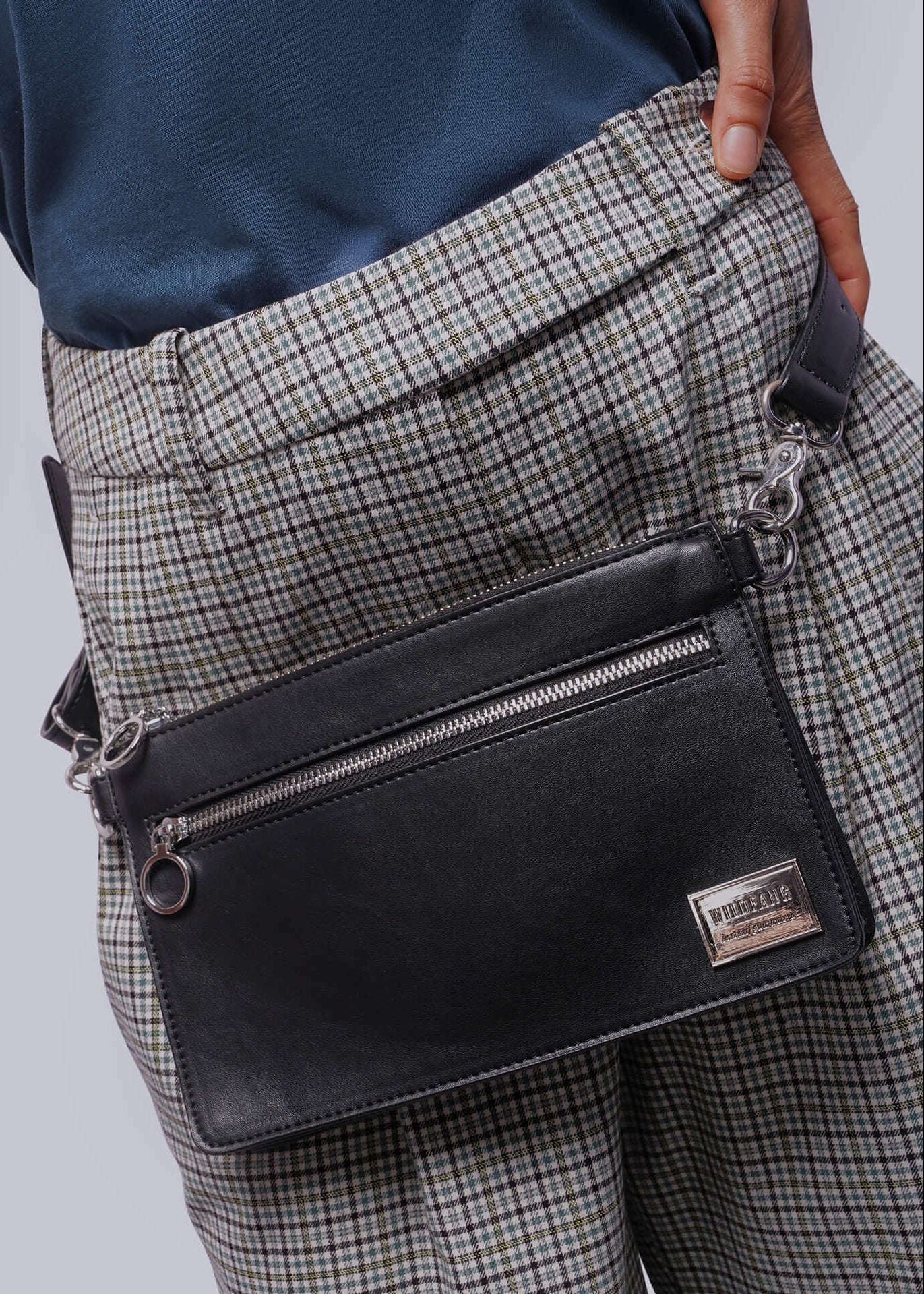 Person wearing a black crossbody bag with a visible brand logo, standing against a neutral background.