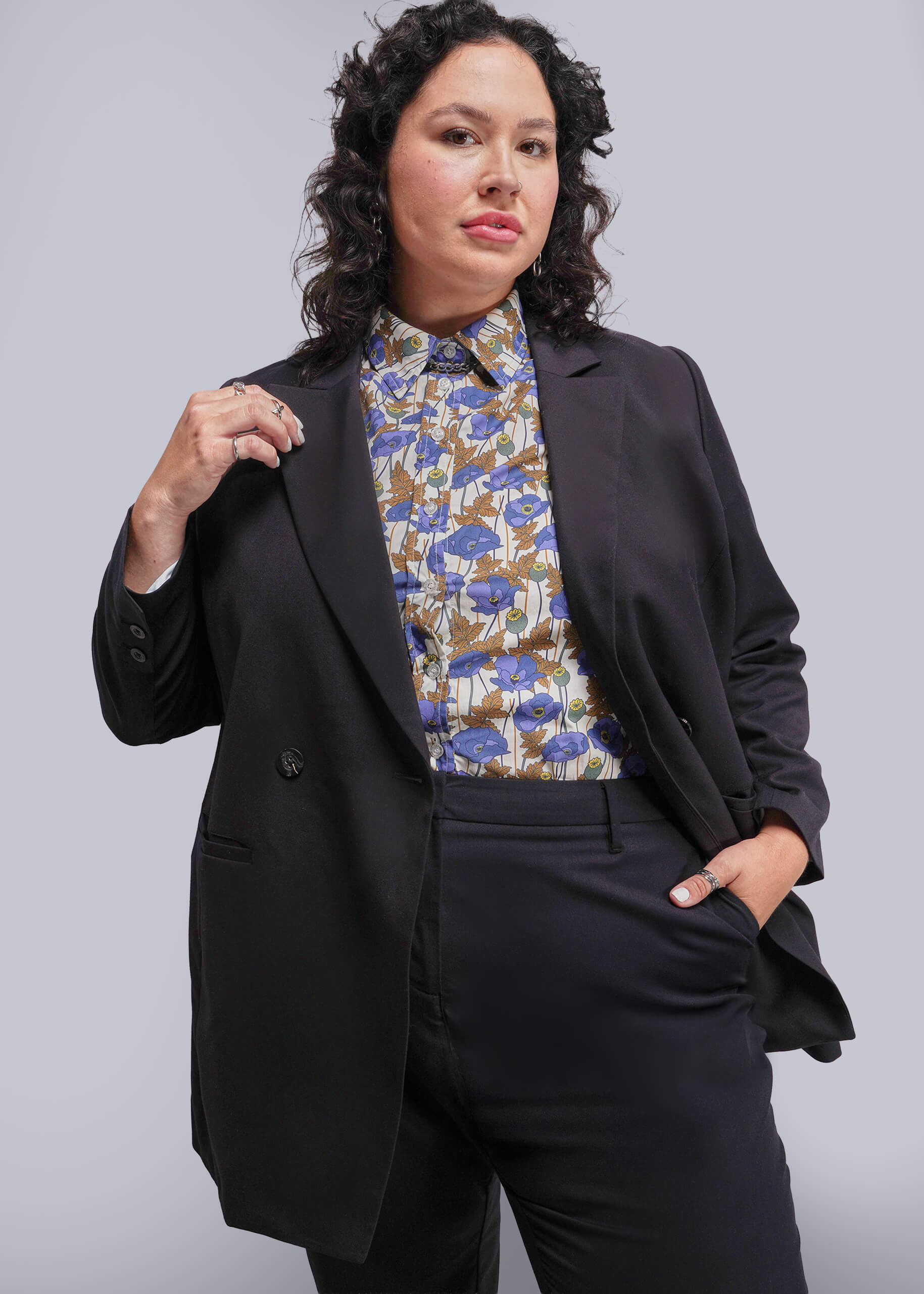 1X=Person wearing a black suit with a floral blouse against a plain background