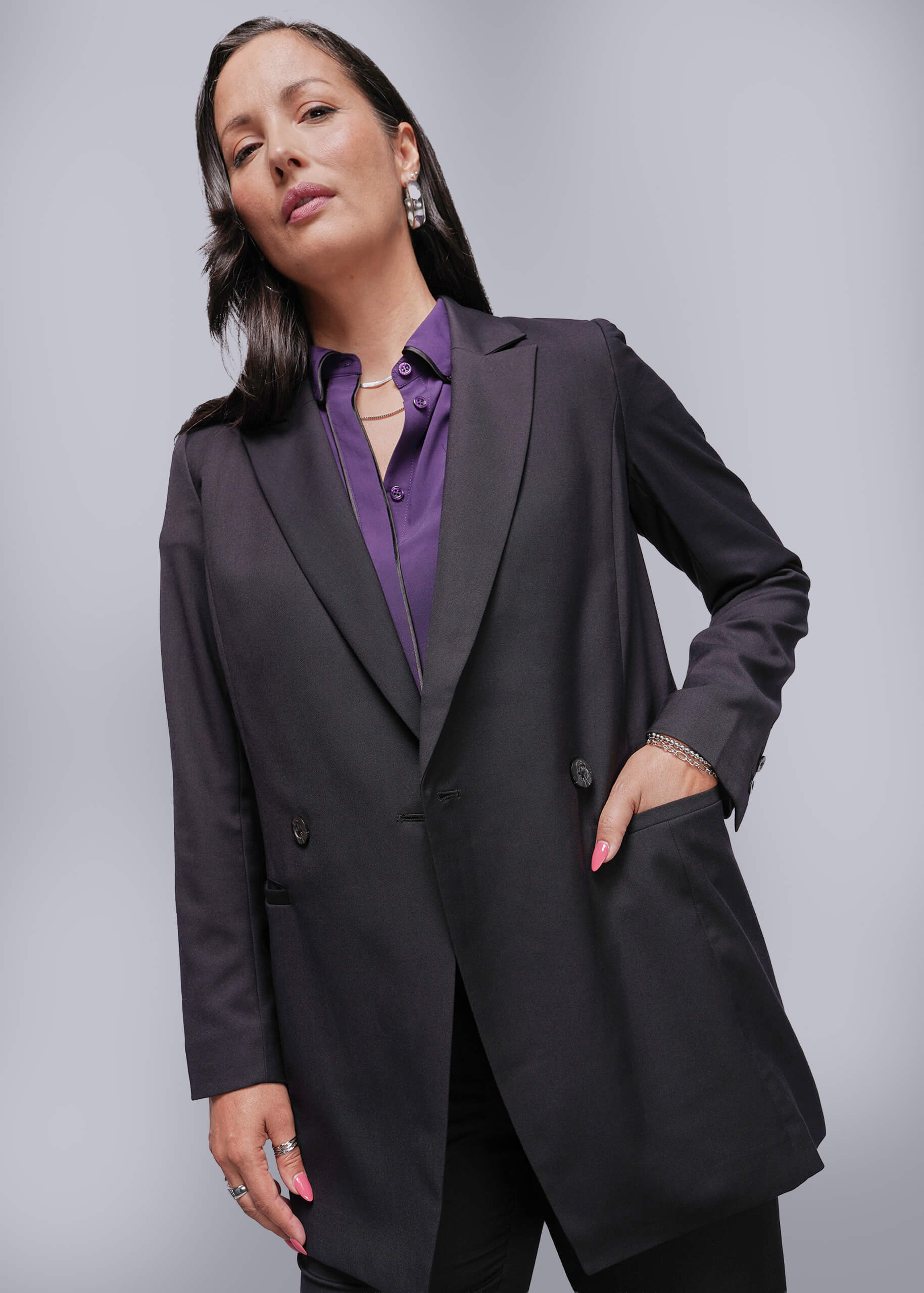 Woman wearing a black blazer over a purple shirt against a gray background