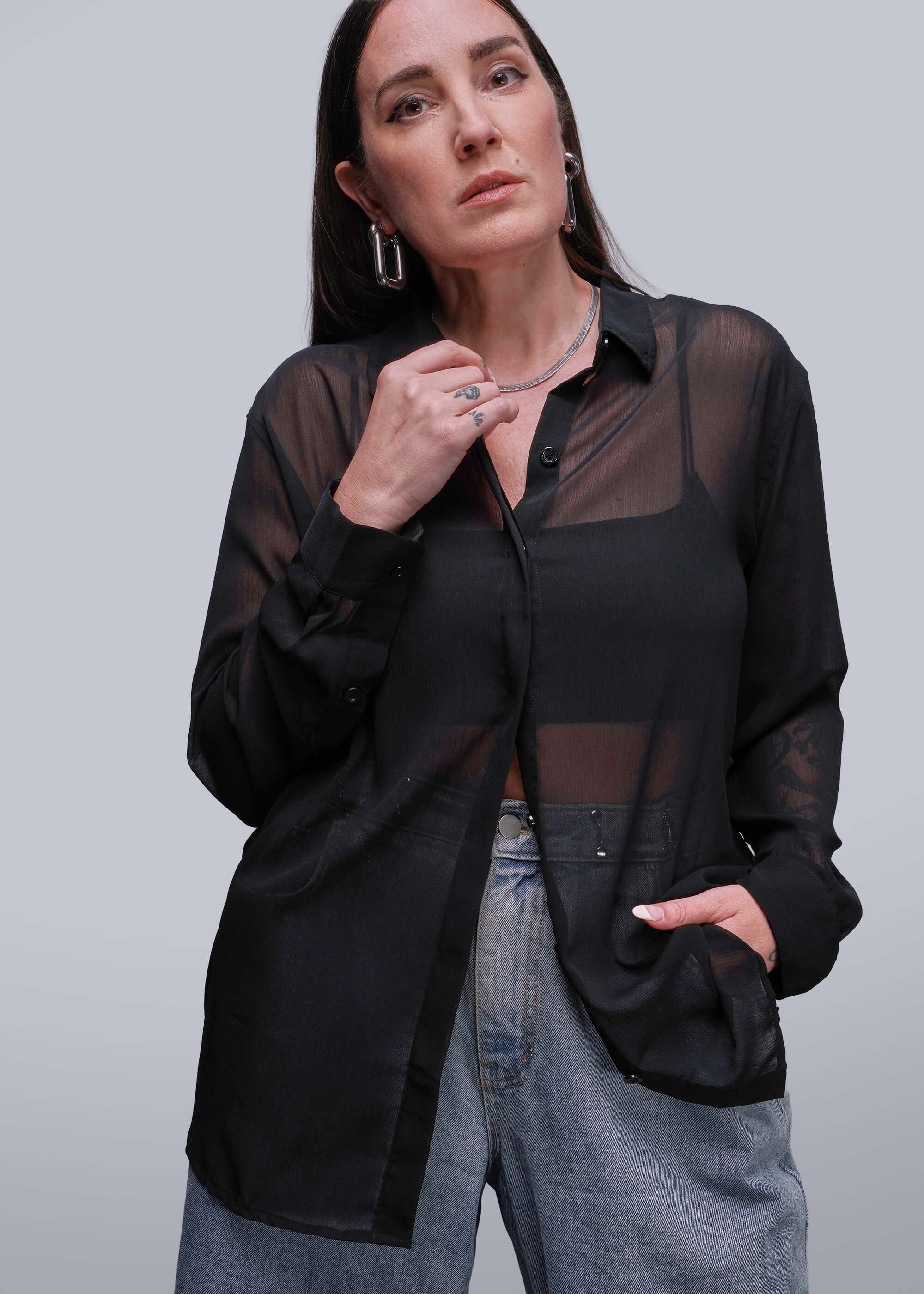 Person wearing a black sheer blouse over a black shirt with gray pants on a light gray background