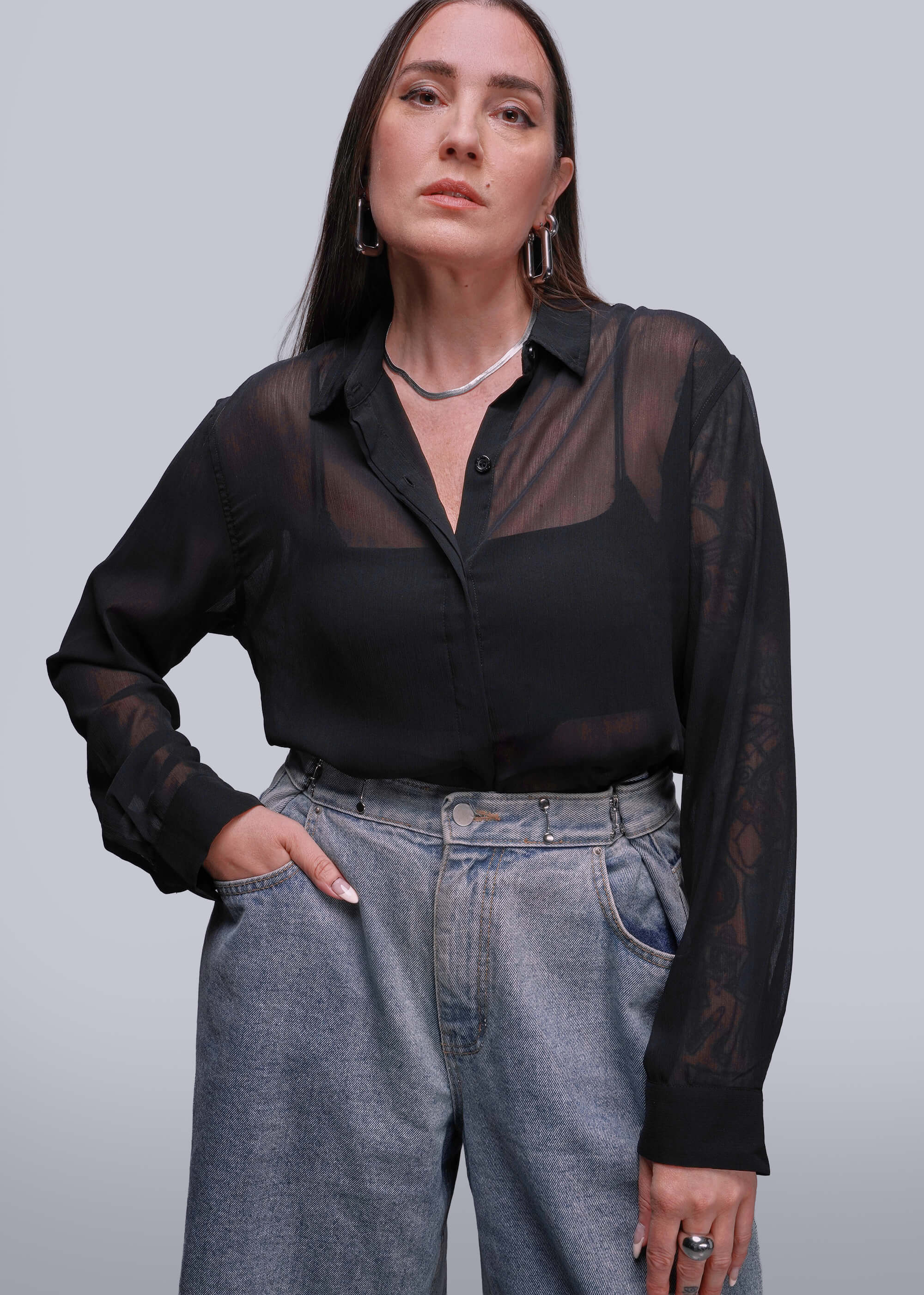 Person wearing a black sheer blouse and gray jeans against a plain background