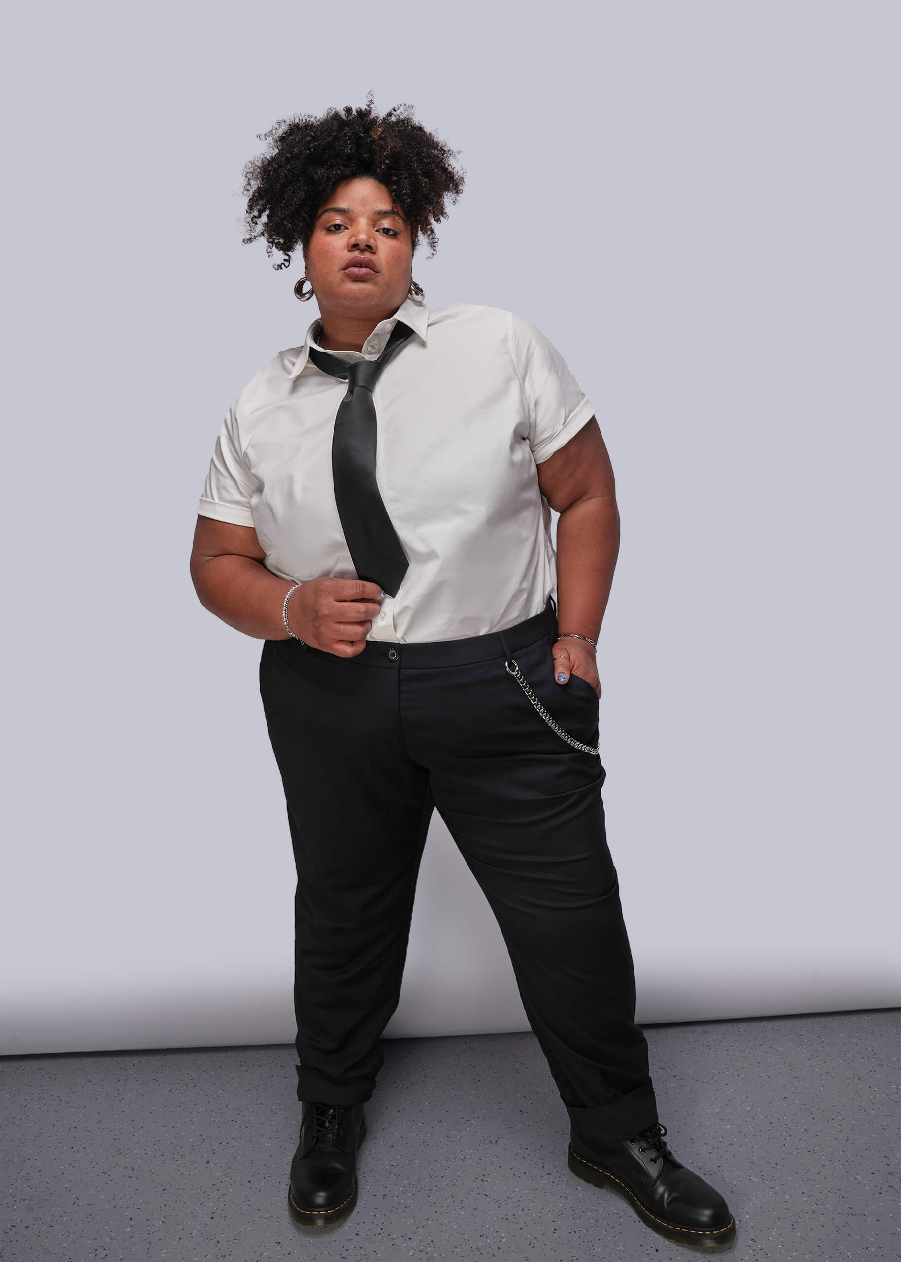 1X=Person wearing a white shirt, black tie, and black pants against a plain background