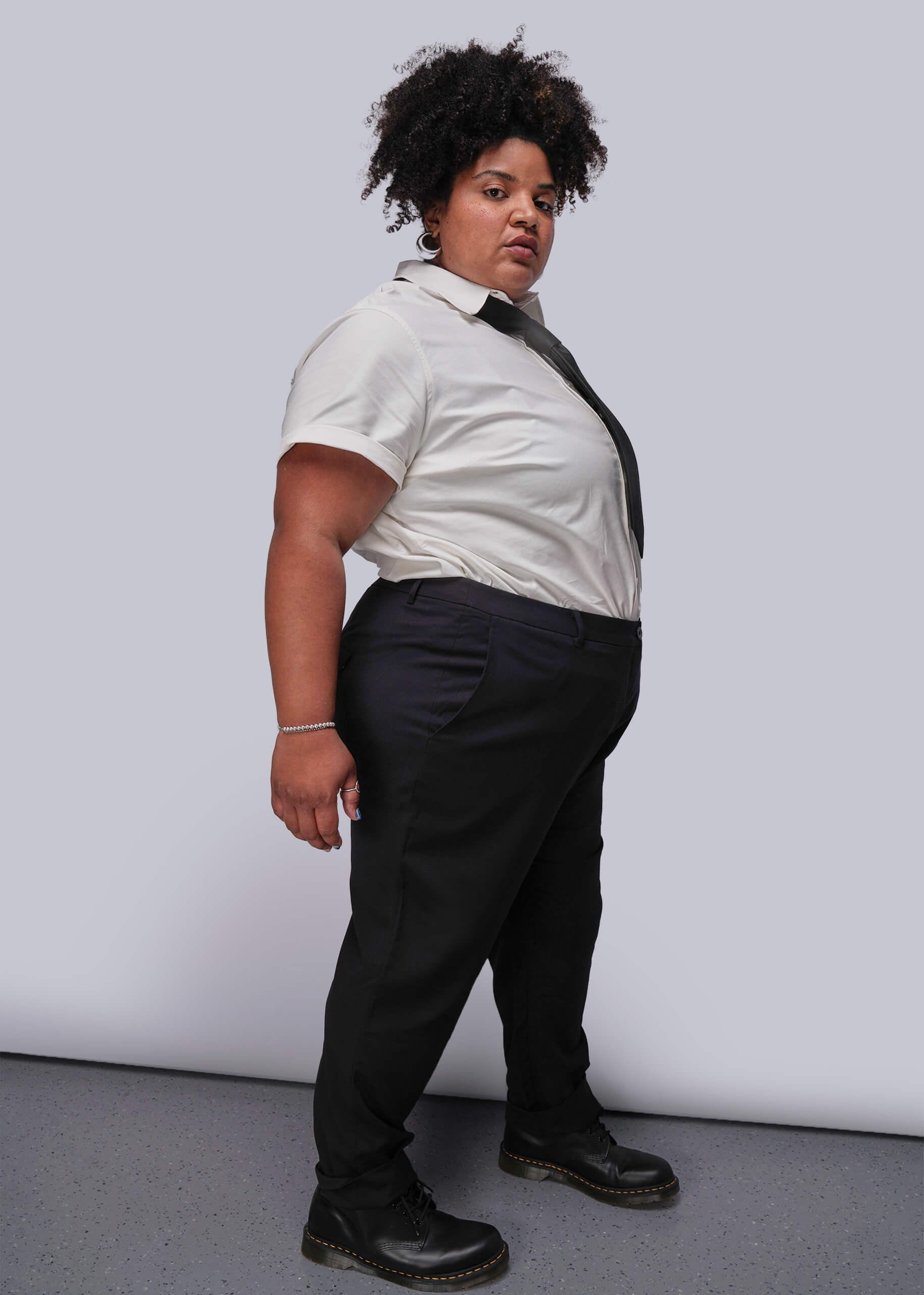 1X=Person wearing a white shirt, black tie, and black pants against a plain background