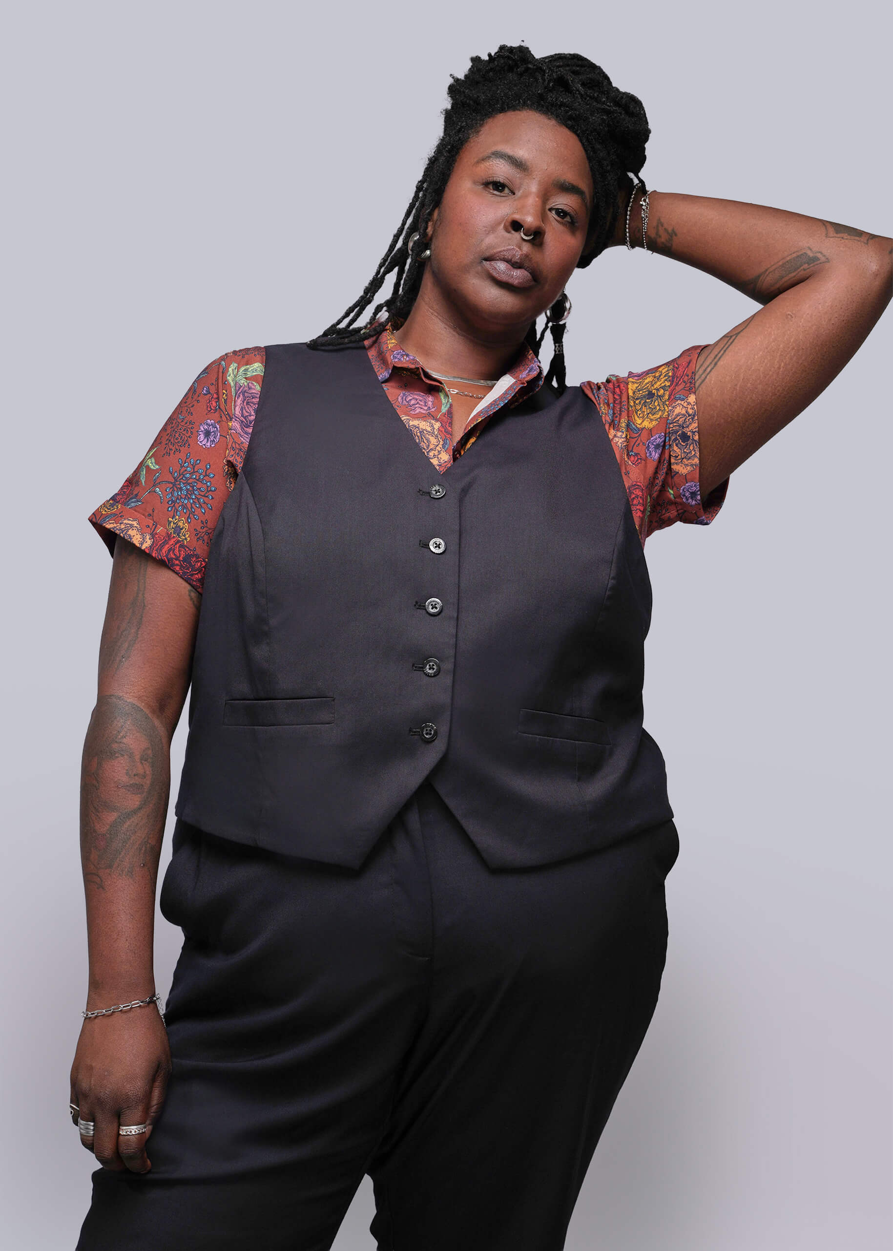 1X=Person wearing a black vest over a patterned shirt with a plain background