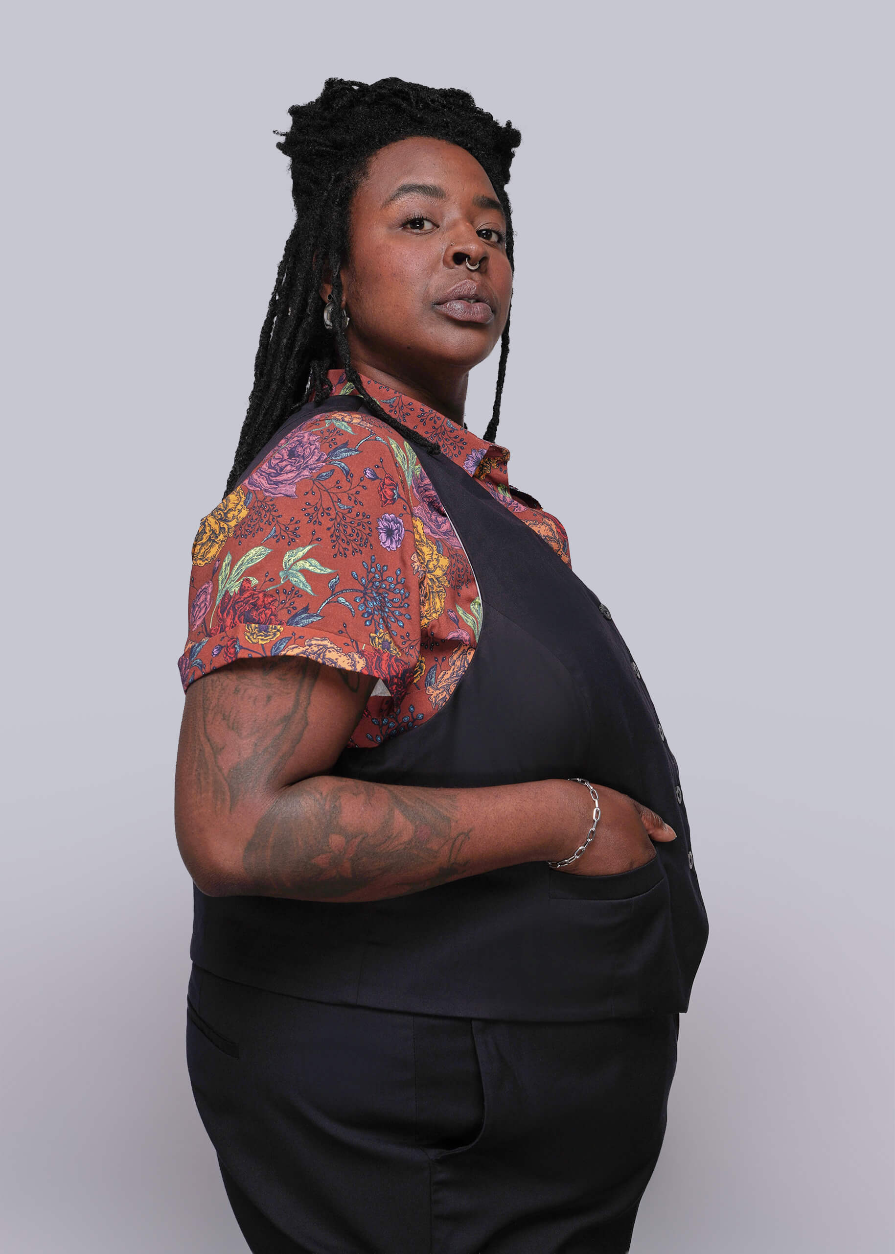 1X=Person wearing a black outfit with a colorful floral shirt over the shoulders against a white background