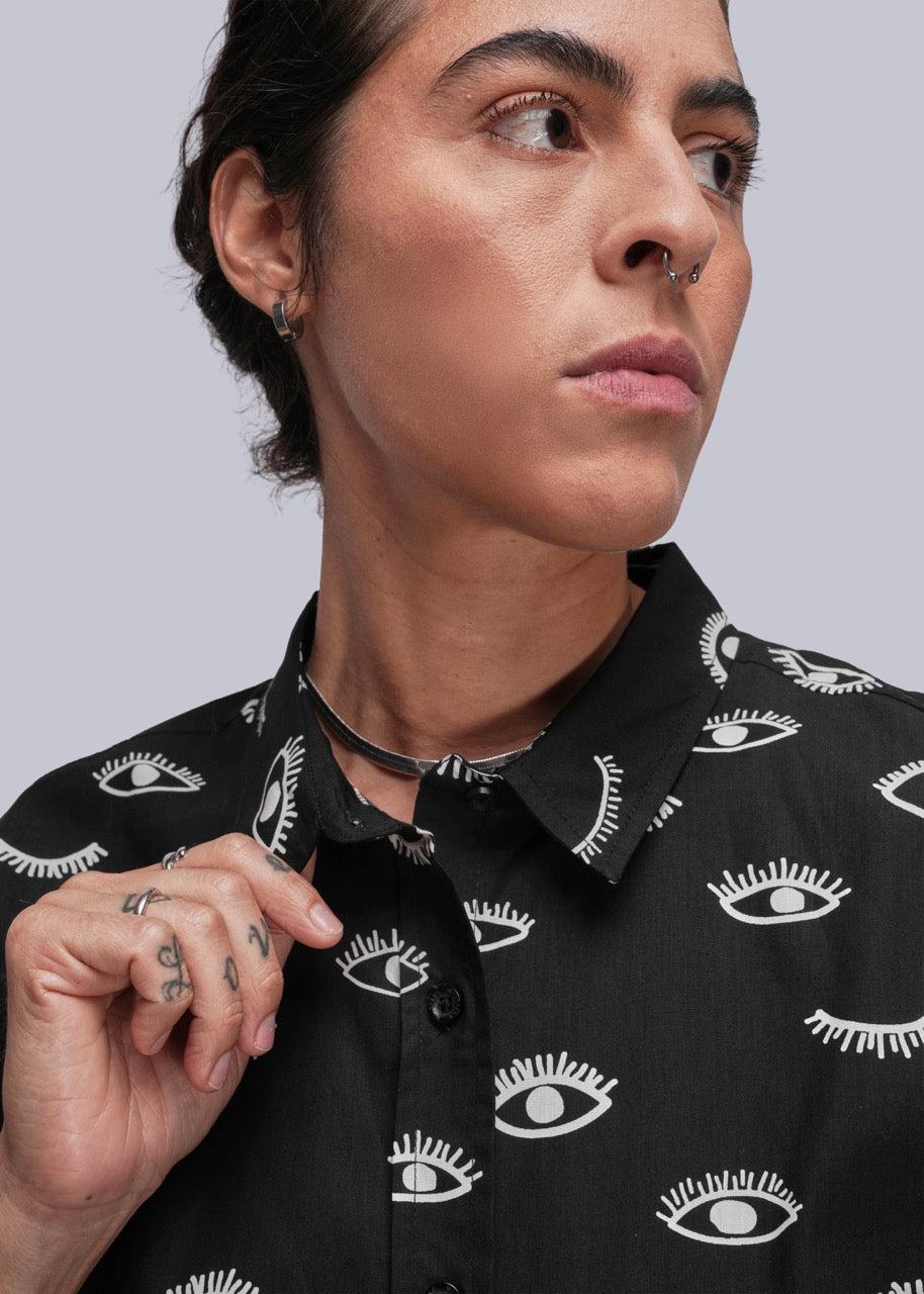 S=Person wearing a black shirt with white eye pattern against a gray background