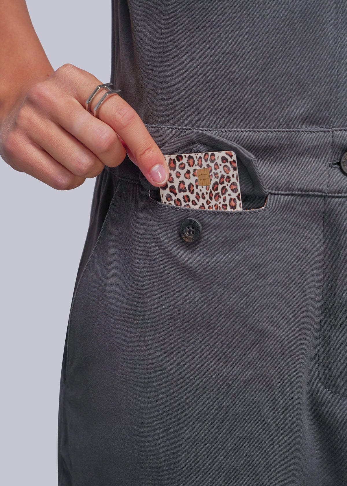 S=Close-up of a person's hand reaching into a side pocket of a dark gray apron, showing a leopard-print card inside the pocket.