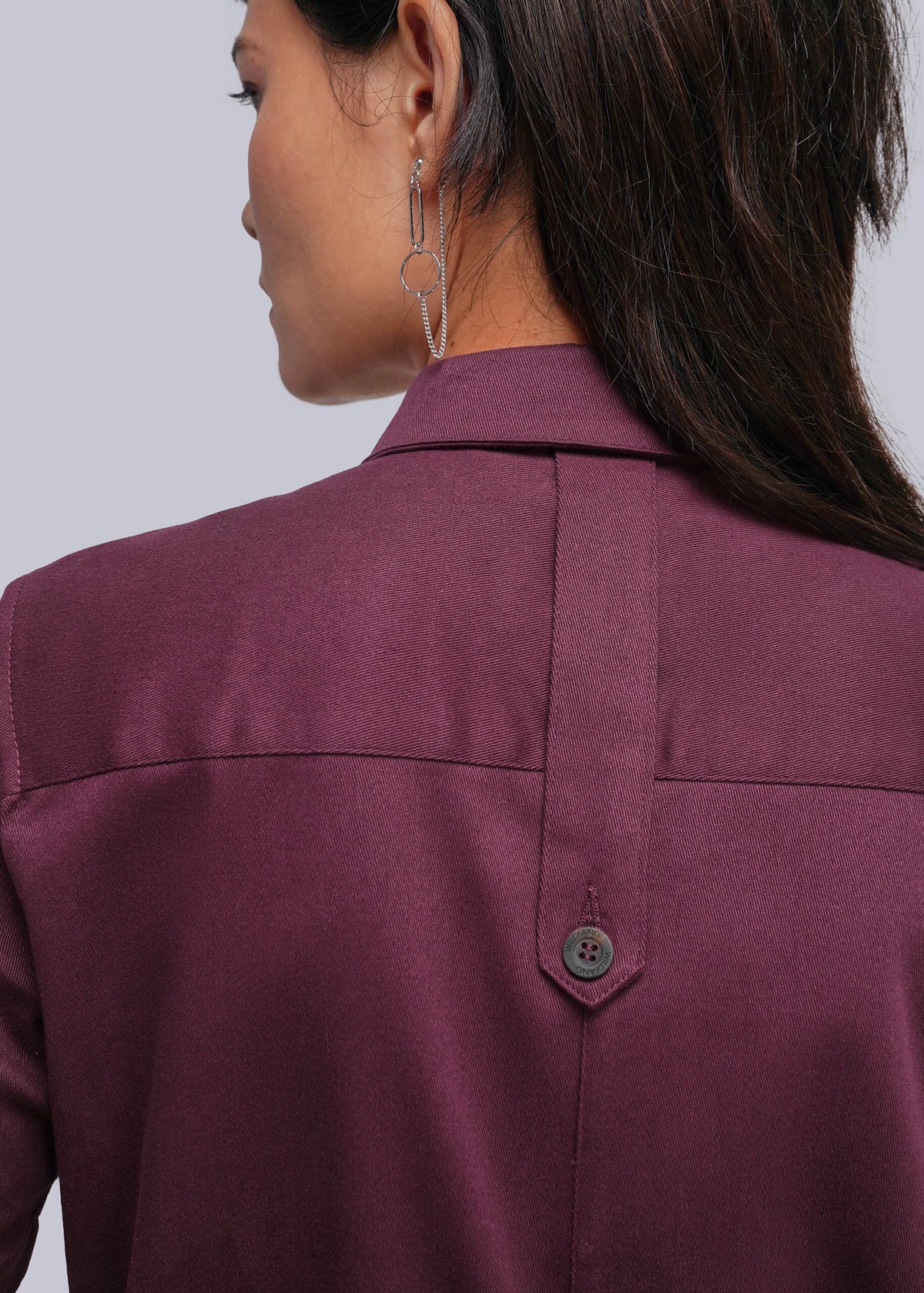 S=Close-up back view of a woman wearing a burgundy jumpsuit, showing the collar, shoulder seams, and a button locker loop detail on the back.