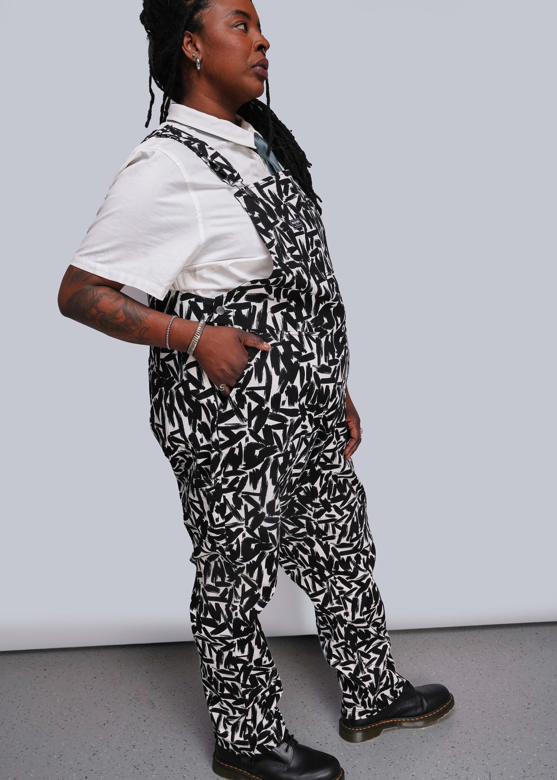 1X=Person wearing a black and white patterned overalls with white shirt underneath against a plain background