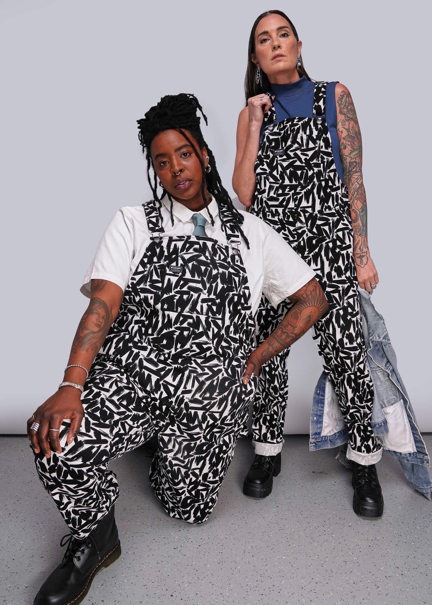Two people wearing black and white patterned overalls against a plain background