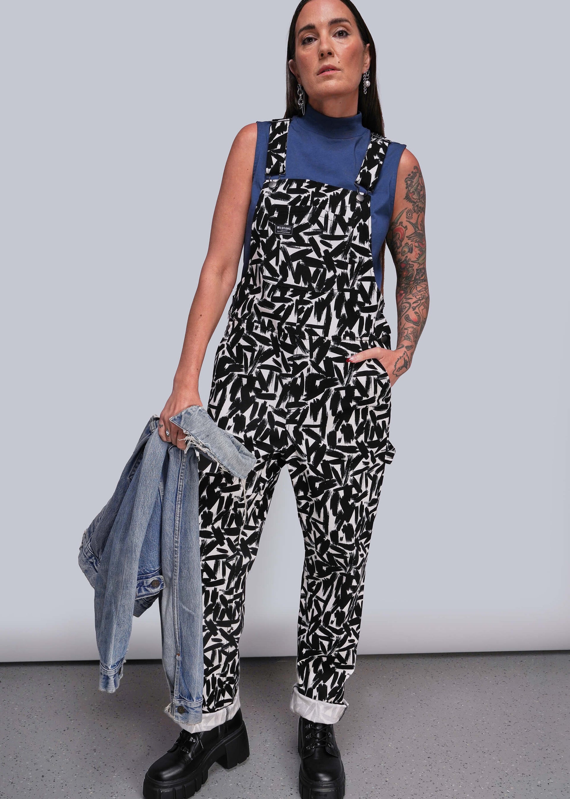 S=Person wearing a patterned jumpsuit holding a denim jacket against a plain background