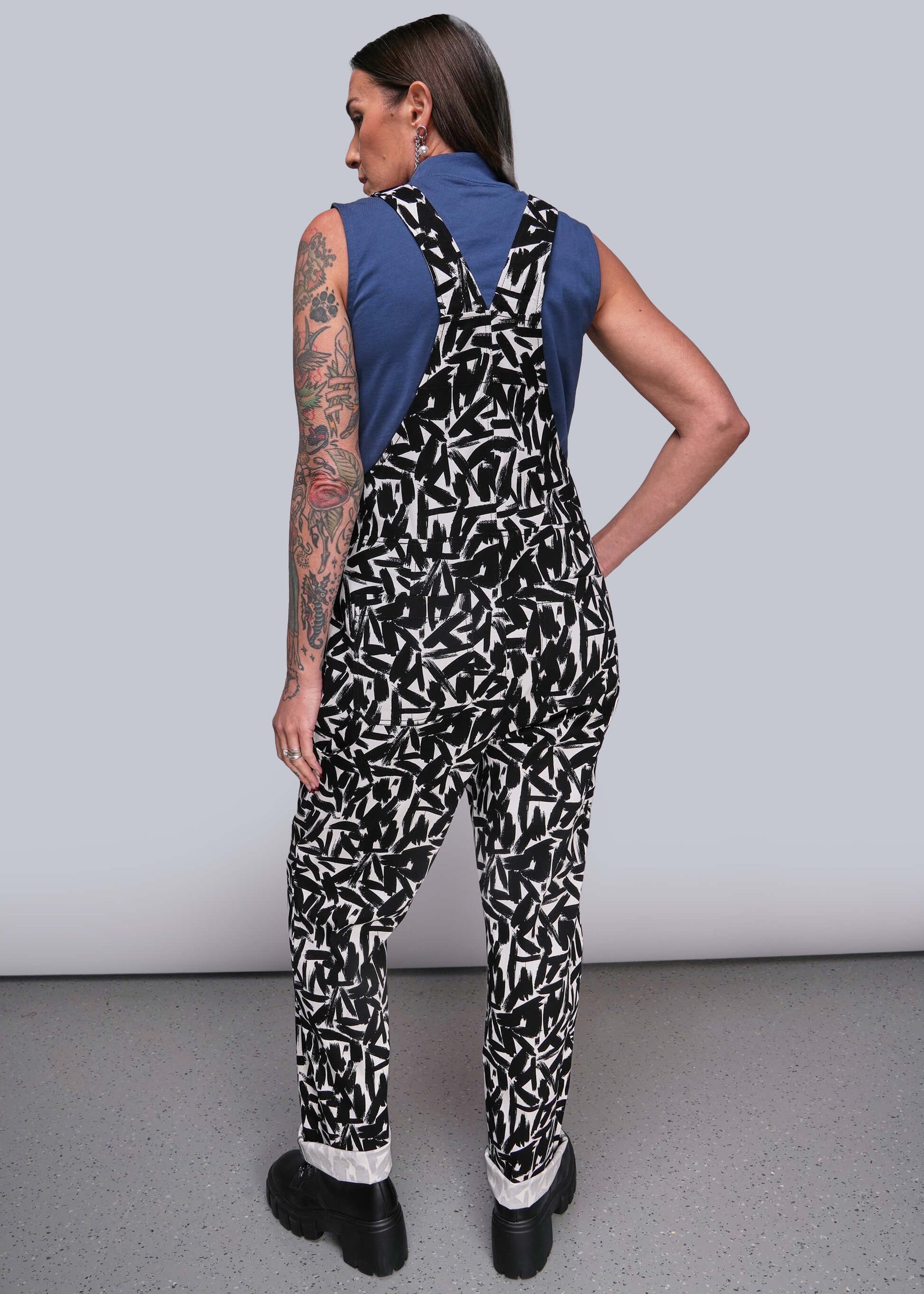S=Person wearing a black and white patterned jumpsuit with a blue top against a gray background