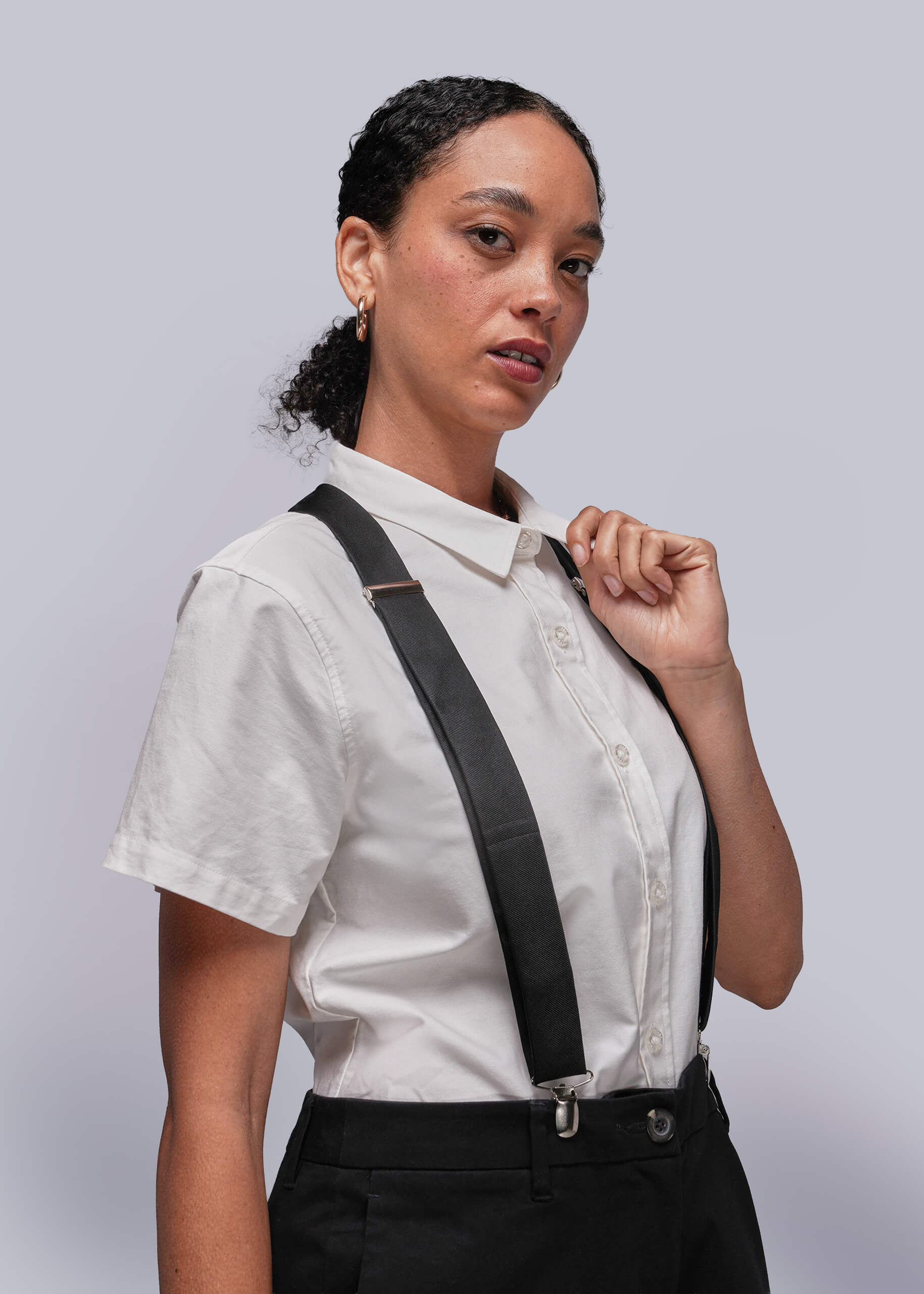Person wearing a white shirt and black suspenders against a light gray background