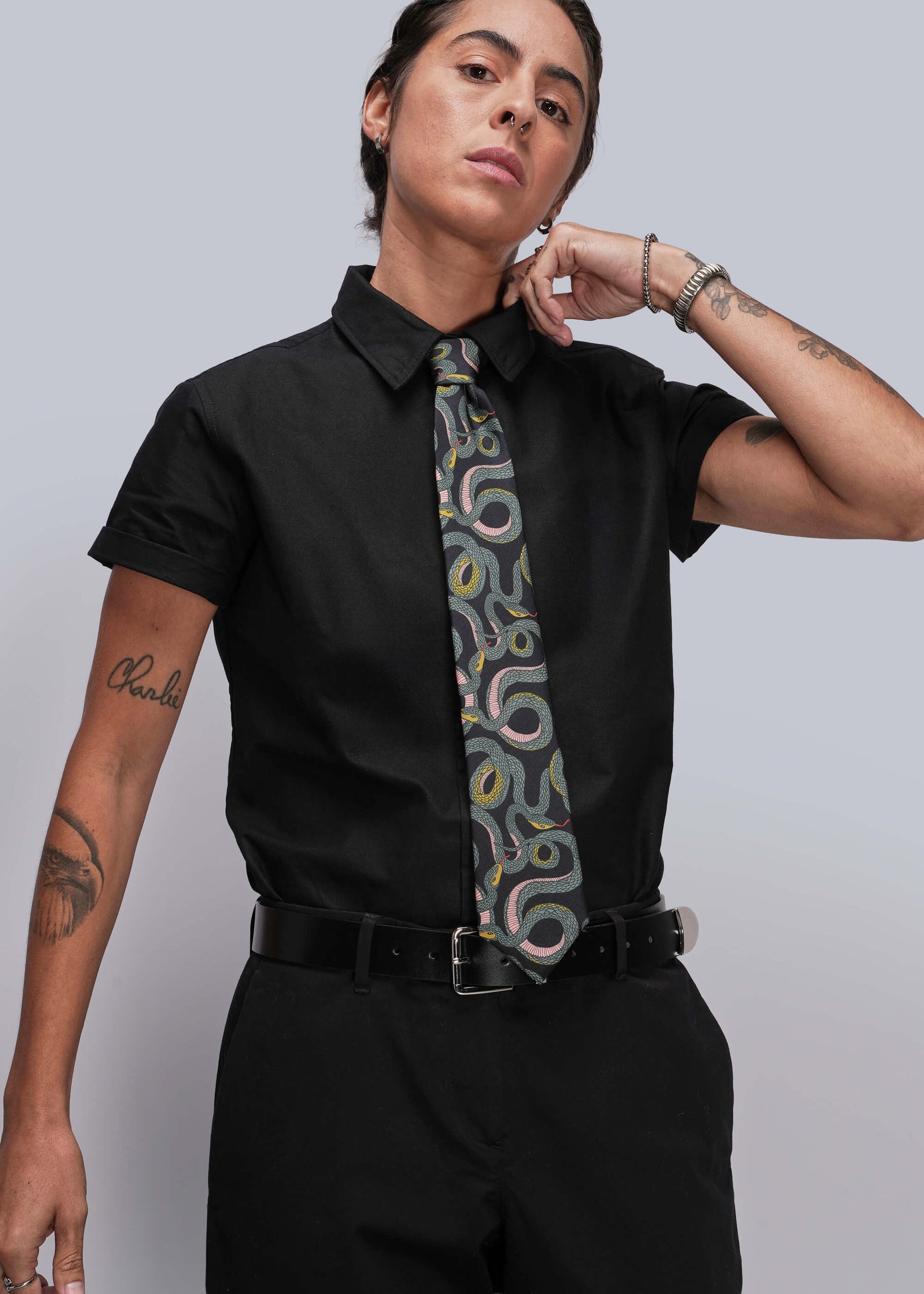 S=Person wearing a black shirt with a patterned tie against a plain background