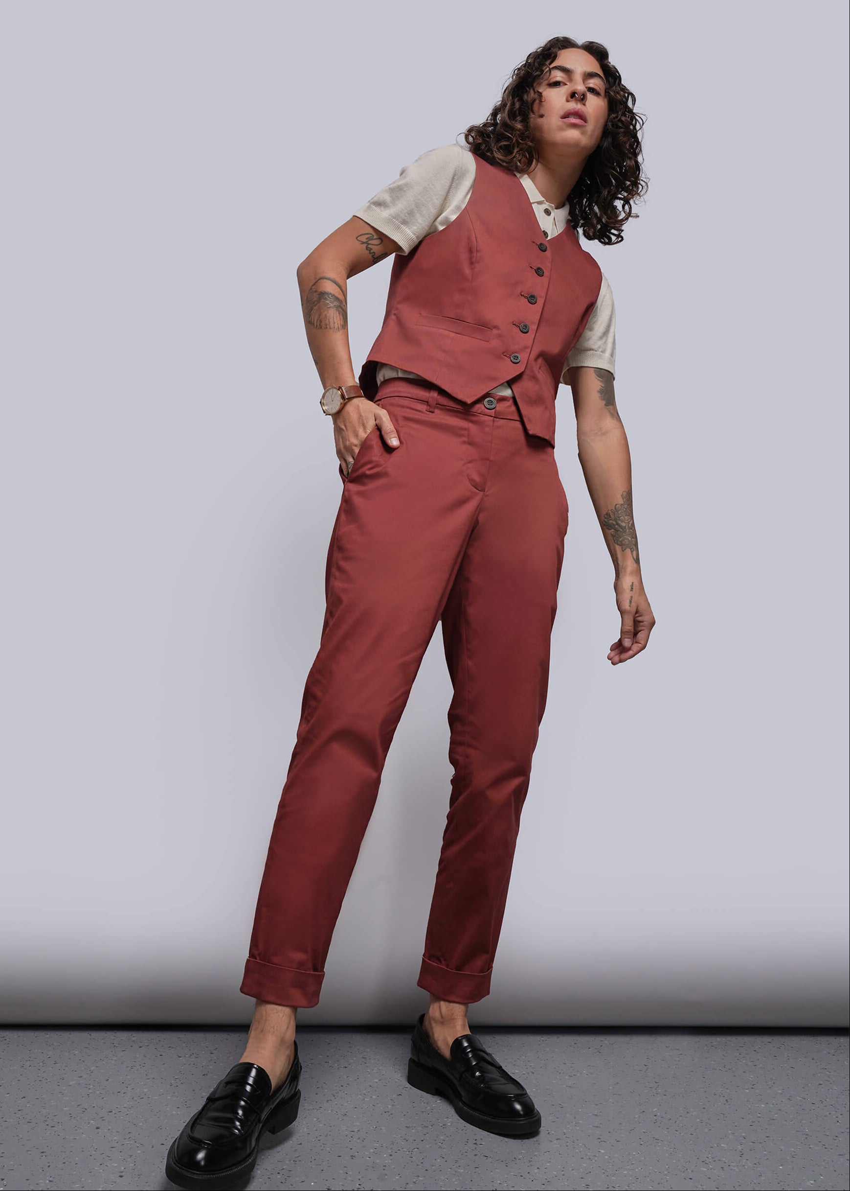 Person wearing a rust colored vest and pants with an off white polo sweater underneath on a plain background