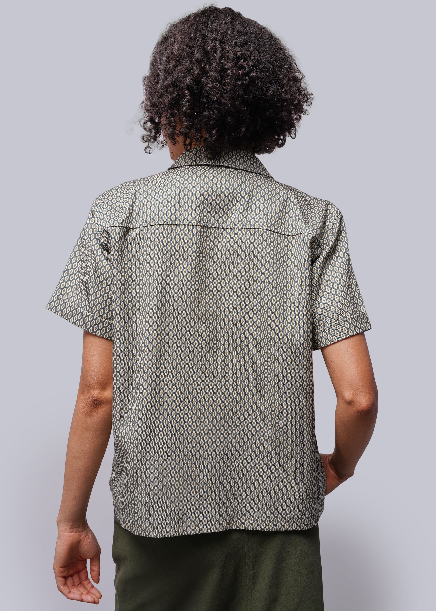 S=Back view of person wearing green patterned button up and green skirt against grey background