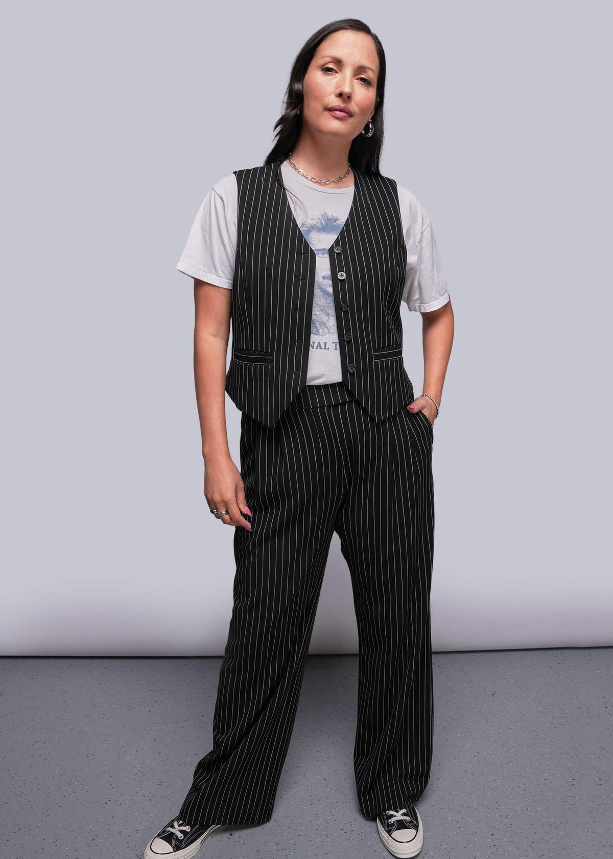 S=Model stands in front of gray background wearing pinstripe vest over t shirt and trouser 