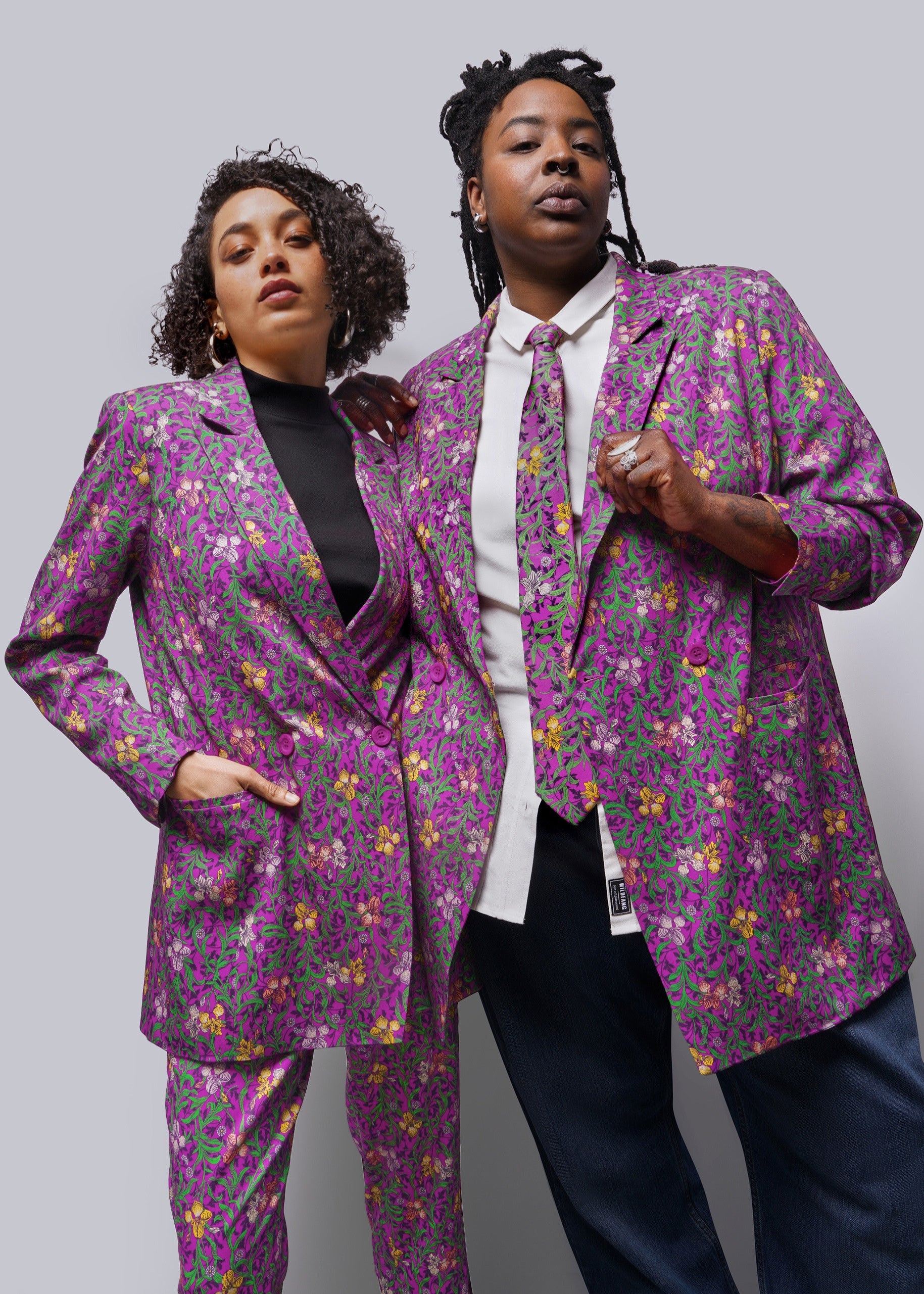 Two people wearing purple printed blazers against grey background