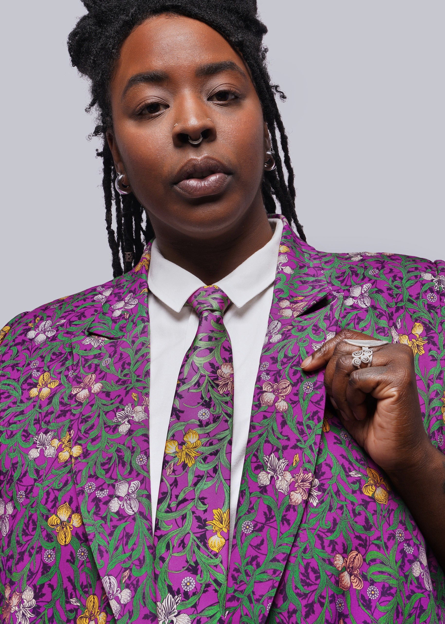 1X=Person wearing a vibrant purple floral suit against a gray background