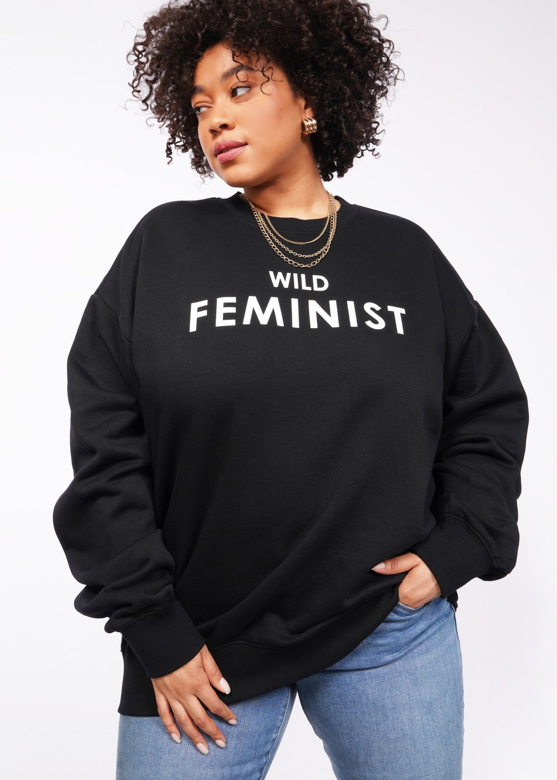 1X=Against a plain white backdrop, someone sports the Wild Feminist Fleece Crew in black. The chic look is accentuated by bold WILD FEMINIST text, their curly hair, gold hoop earrings, and layered necklaces. The outfit is elevated by the crews soft brushed fleece feel.