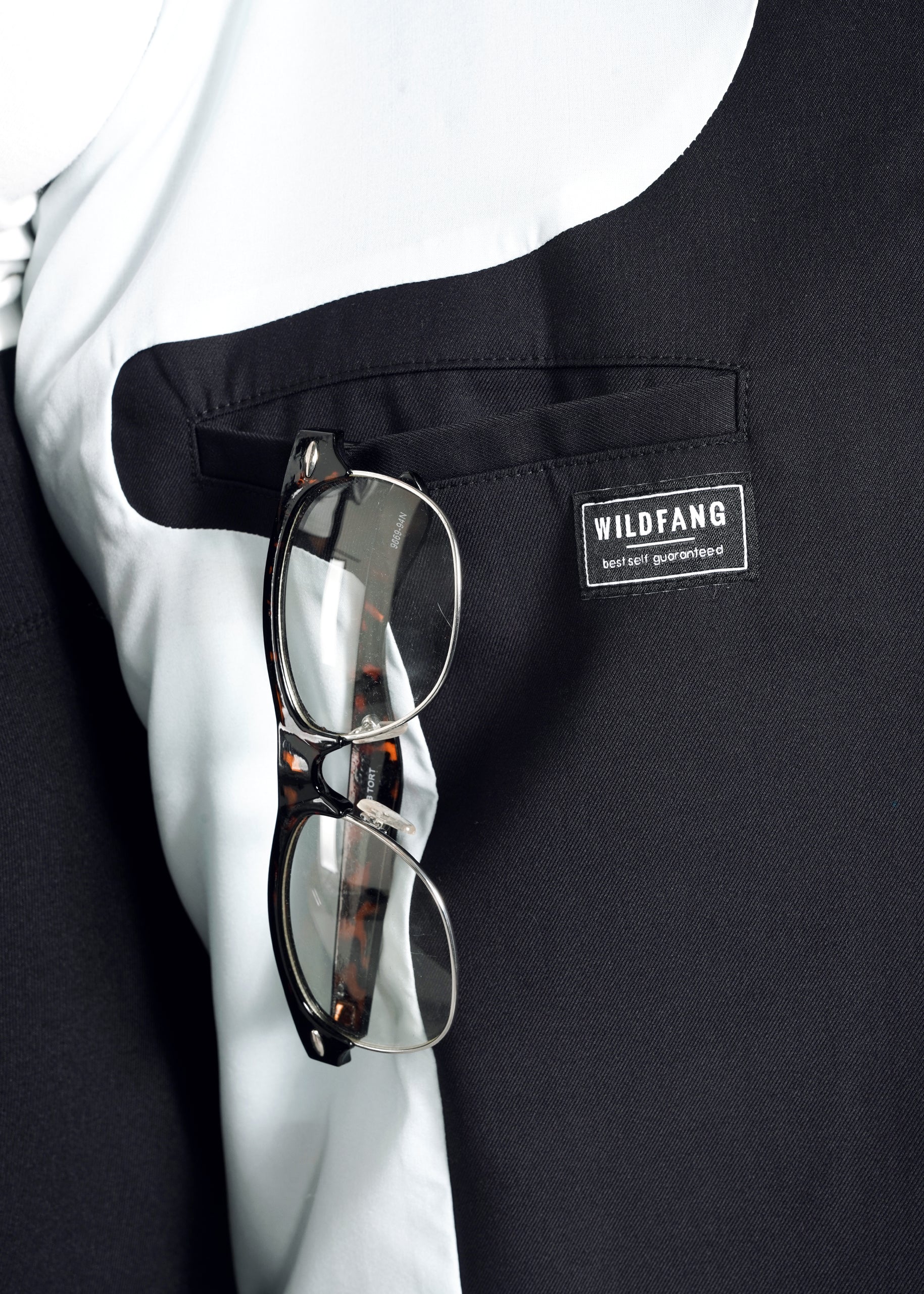 1X=Close-up of The Empower Double Breasted Vest in black and white with an oversized fit, featuring a pocket labeled WILDFANG. Dark-framed glasses are hooked over the pocket, showcasing the brands logo beneath, adding a stylish touch to this bold piece.